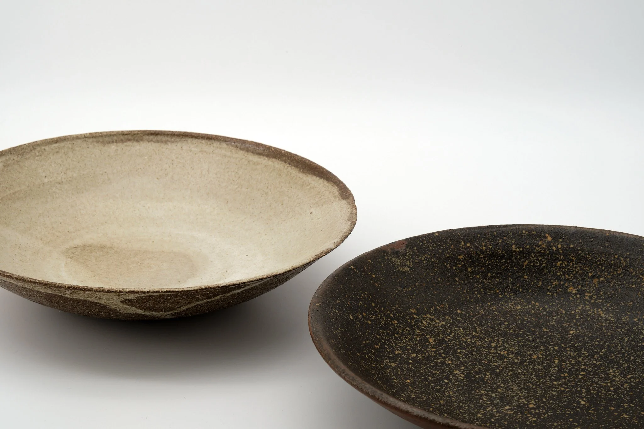 Two ceramic bowls with earthy tones, one light and one dark, against a plain white background.