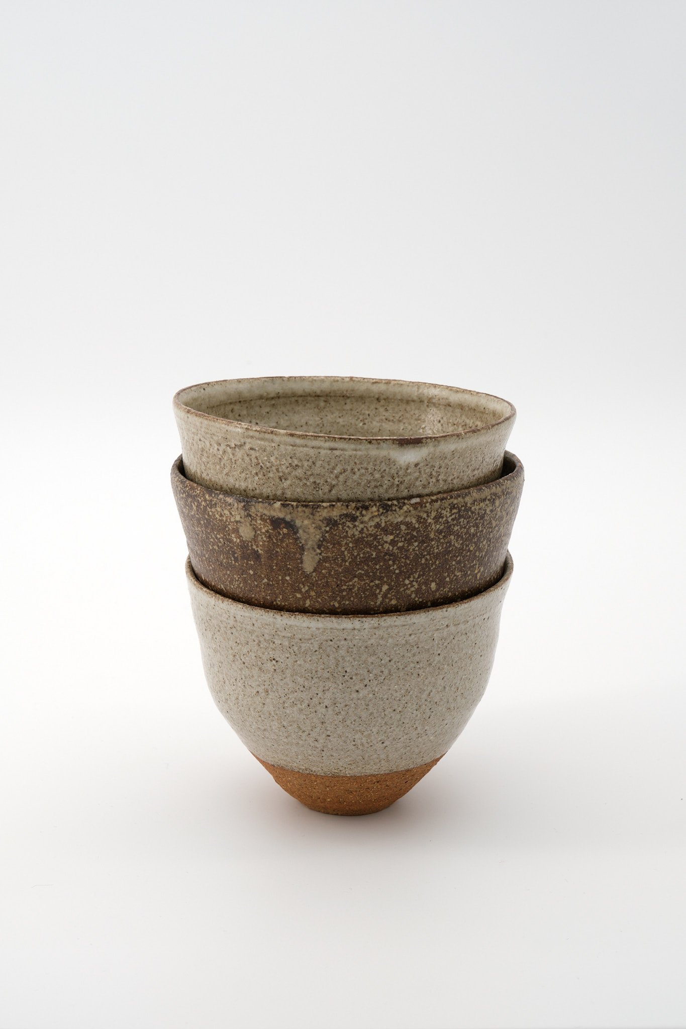A stack of four ceramic bowls with earthy, neutral tones, displayed against a plain white background.