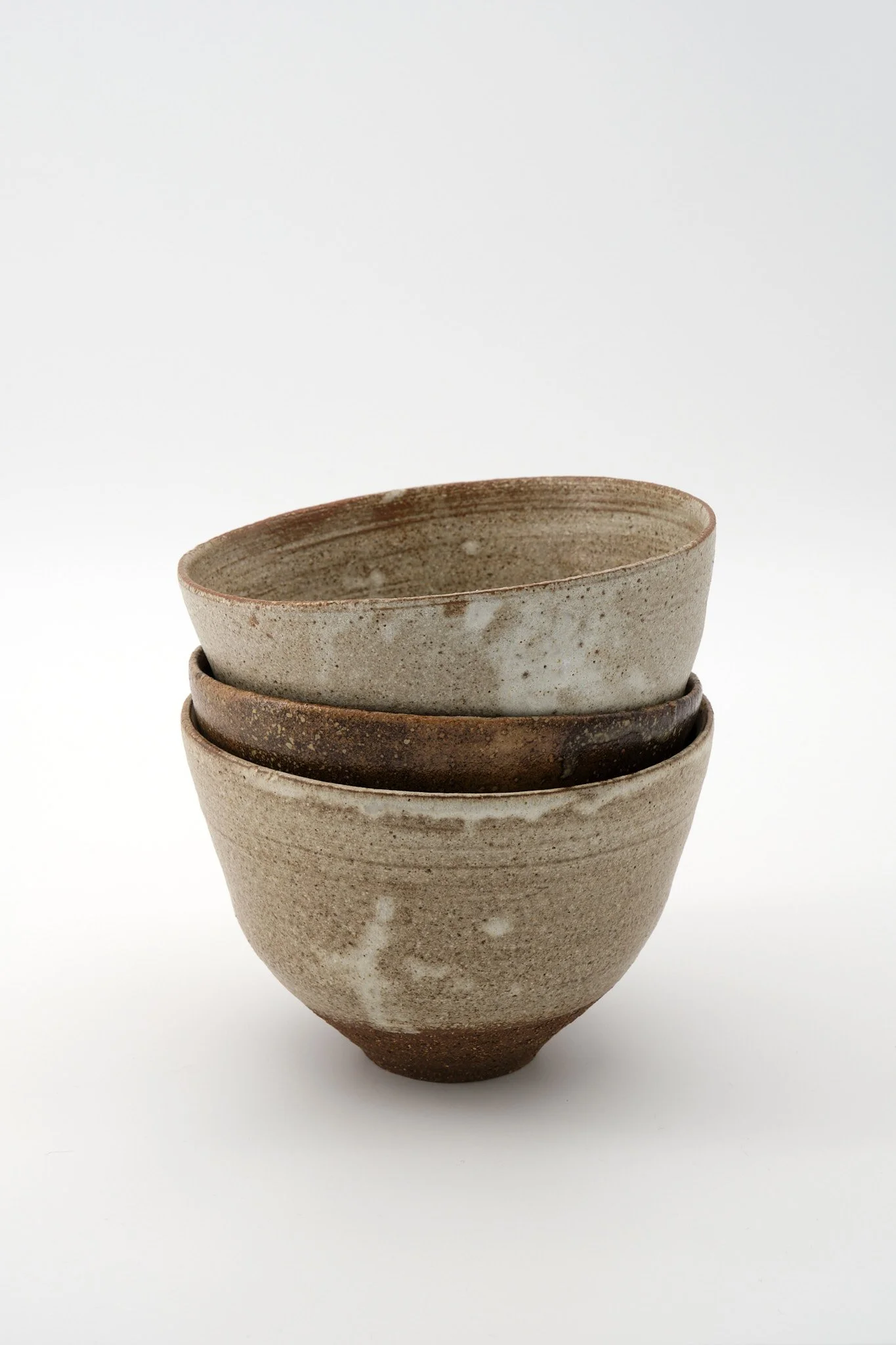 A stack of four ceramic bowls with a natural, earthy finish, arranged against a plain white background.