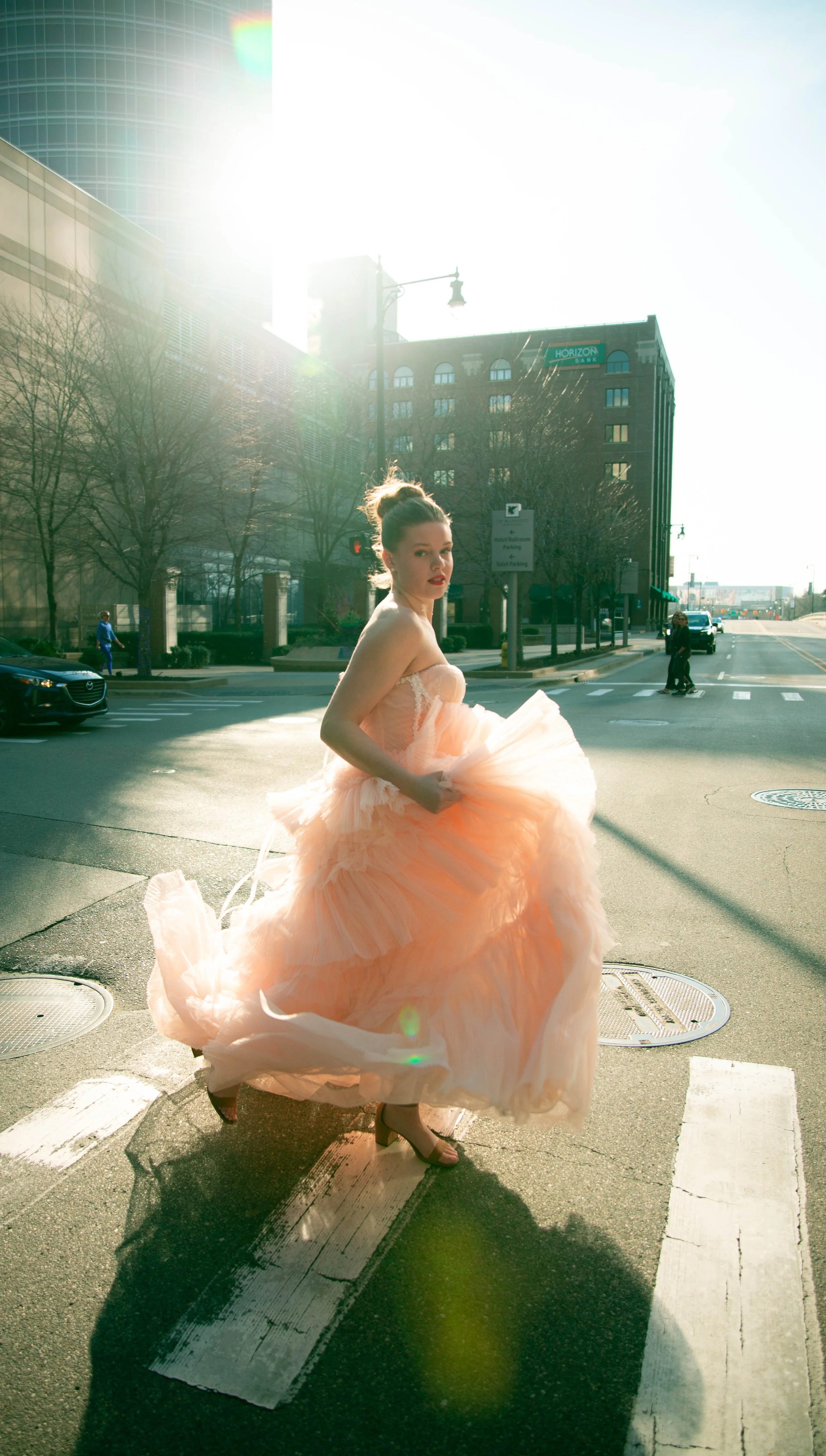 Editorial fashion photo of a model in a peach tulle ball gown running across a downtown Grand Rapids street near the Amway Grand Plaza, by Olivia Feldman Photography