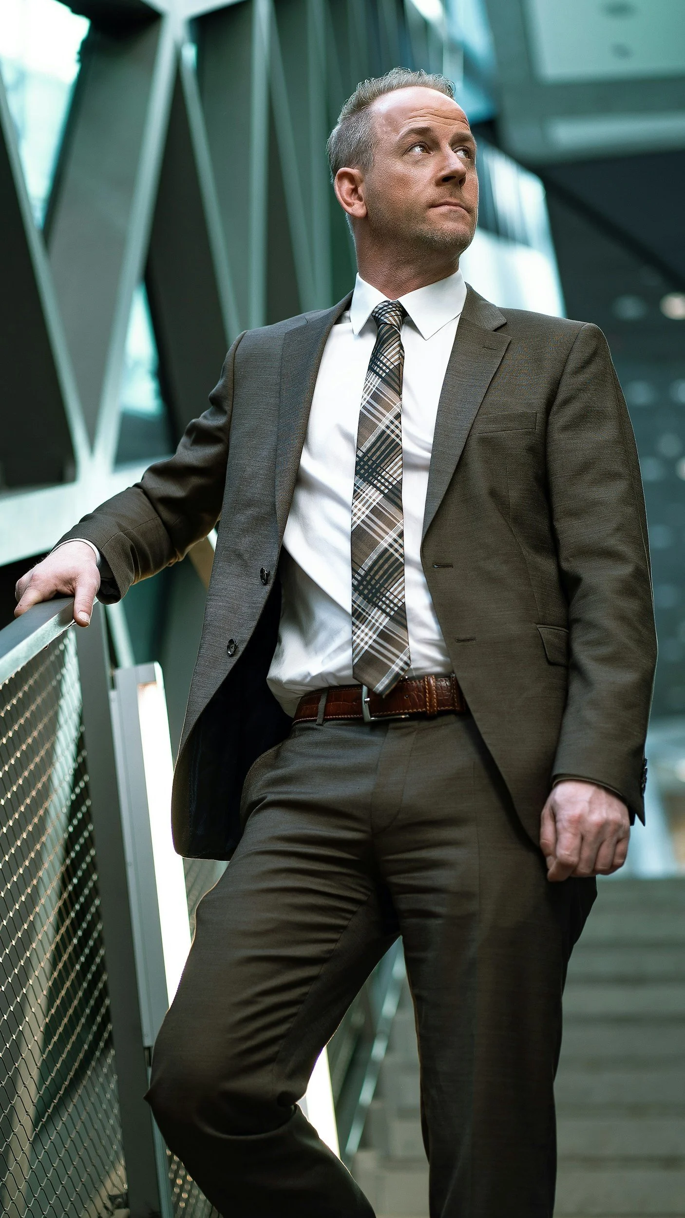 A man in a business suit leaning against a railing in a modern office building.