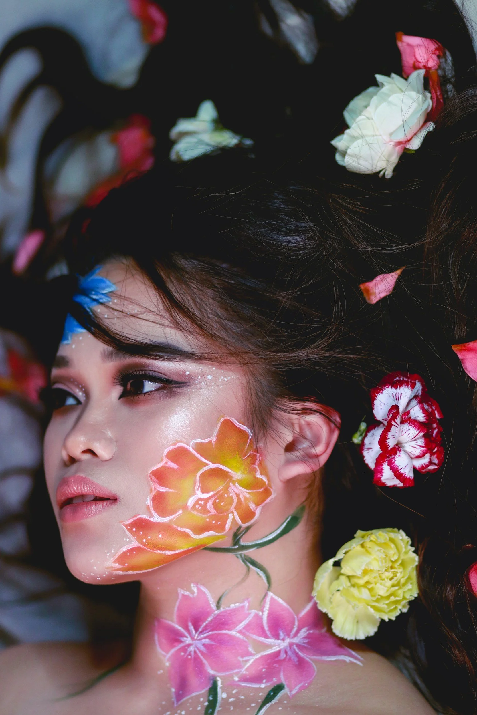 Close-up of a woman's face with intricate floral face paint and colorful flowers in her dark hair