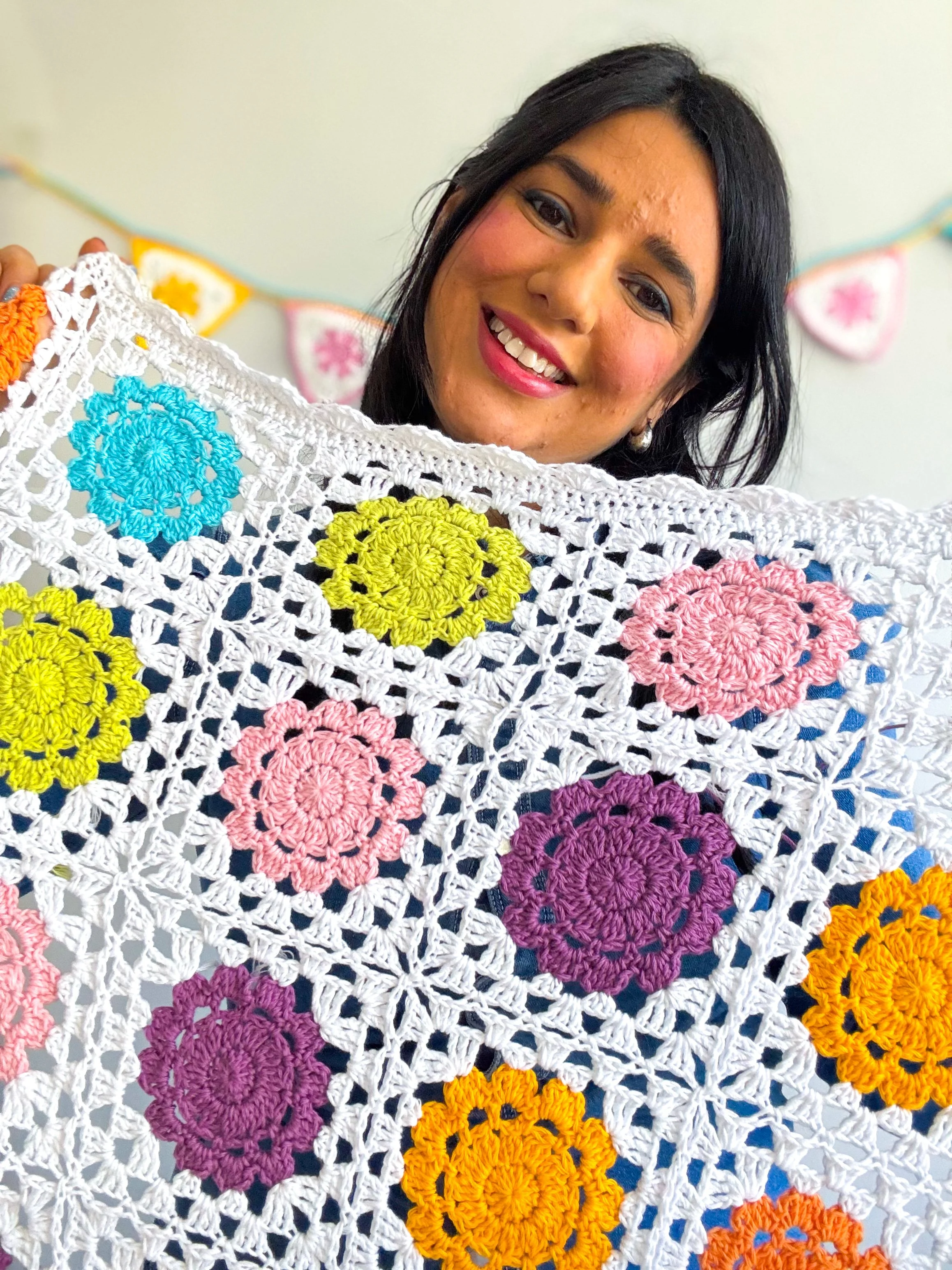 A young woman holding a crochet baby blanket made out of colorful granny squares