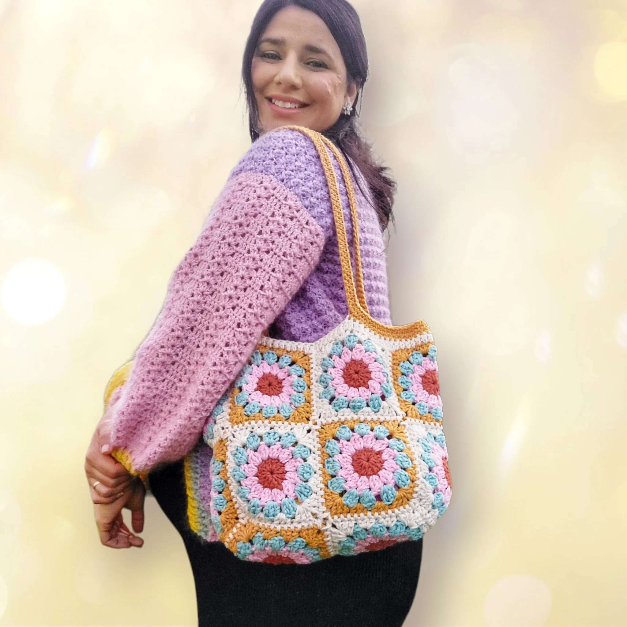 Woman in a pink and purple crocheted sweater carrying a colorful crocheted bag featuring floral patterns.