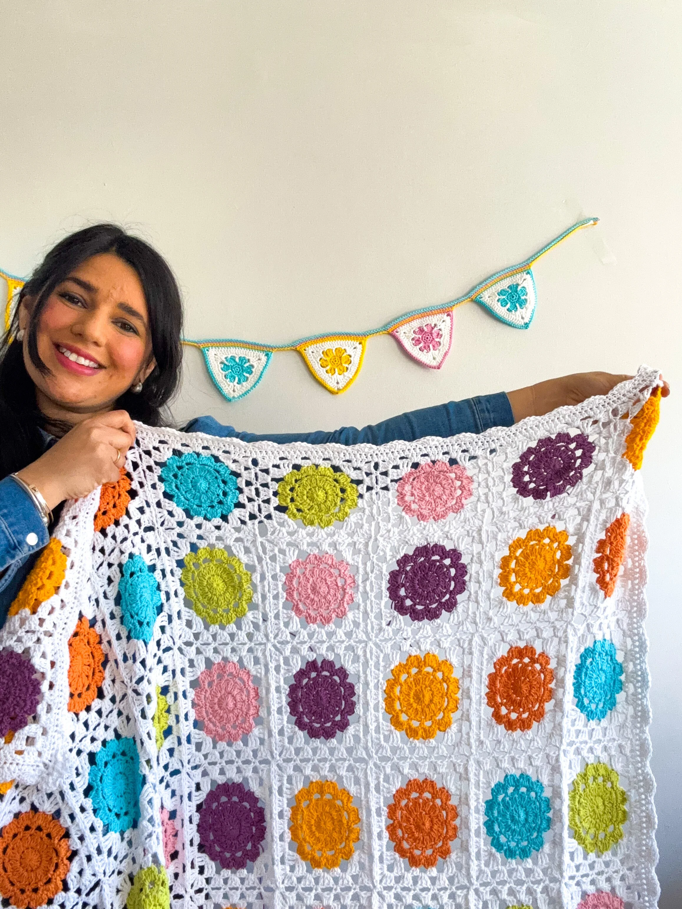 a young woman holding a flower granny square blanket made for babies