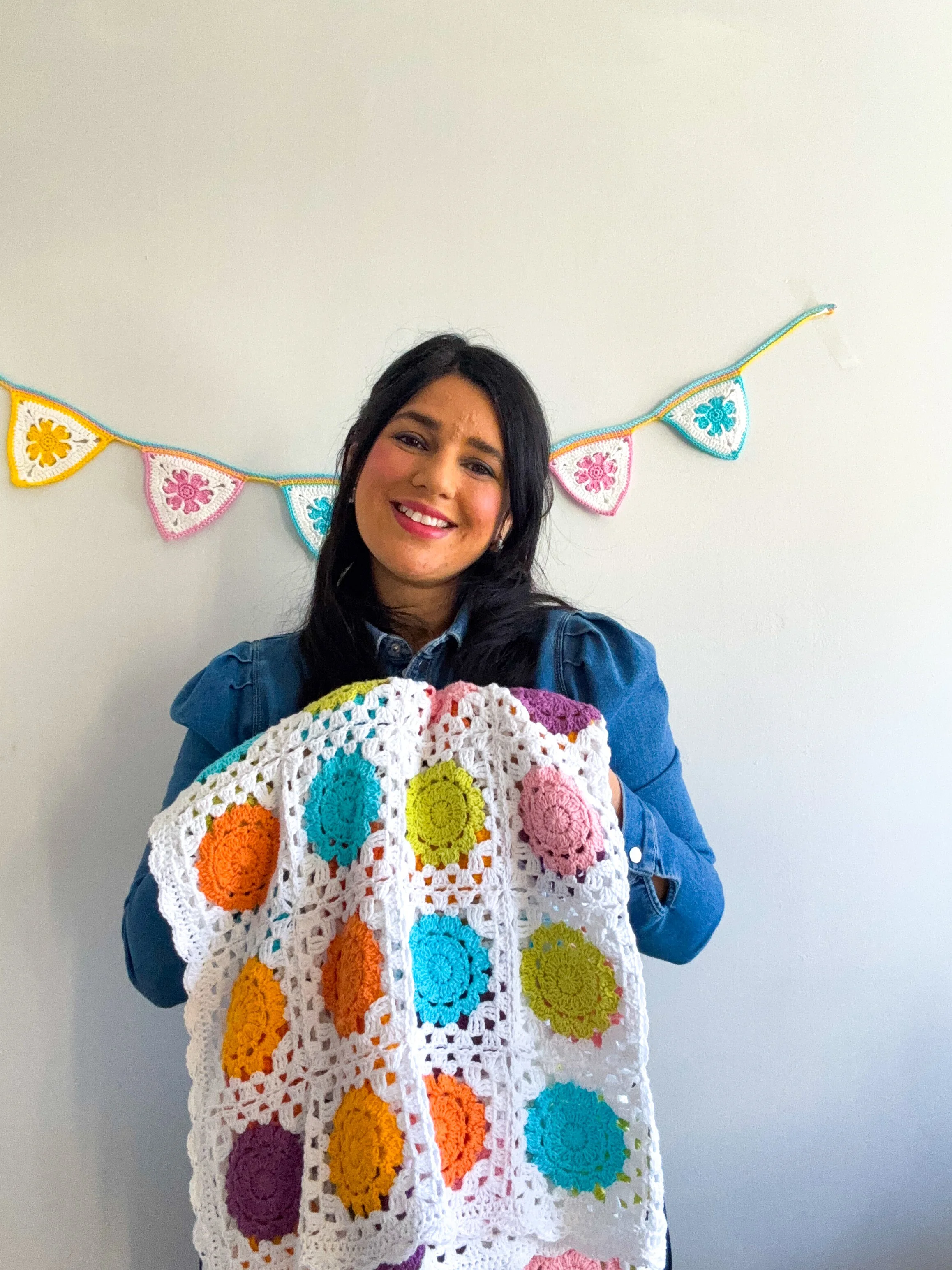 a young woman holding a crochet baby blanket made out of flower granny squares