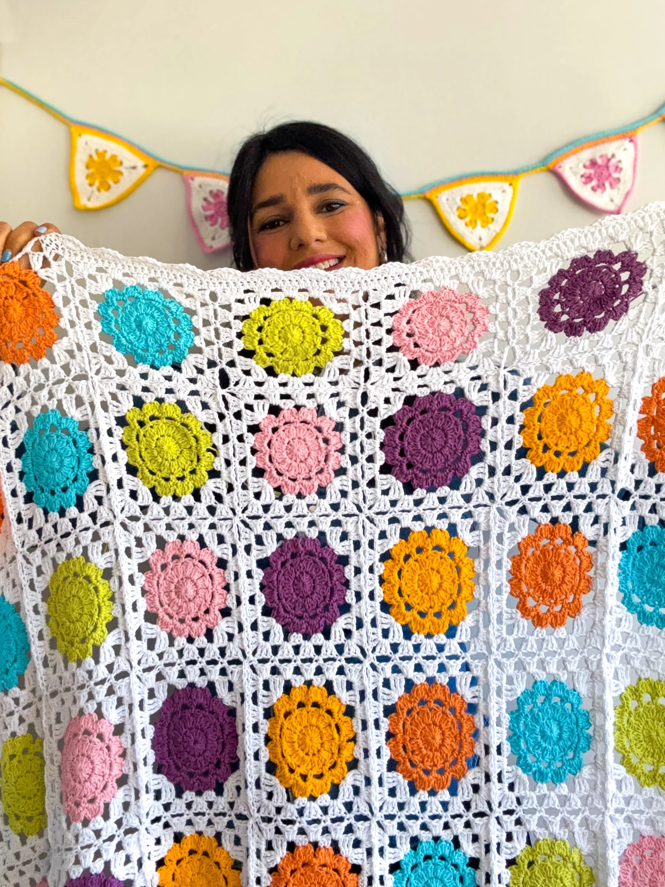 a woman holding a crochet flower granny square blanket made for babies