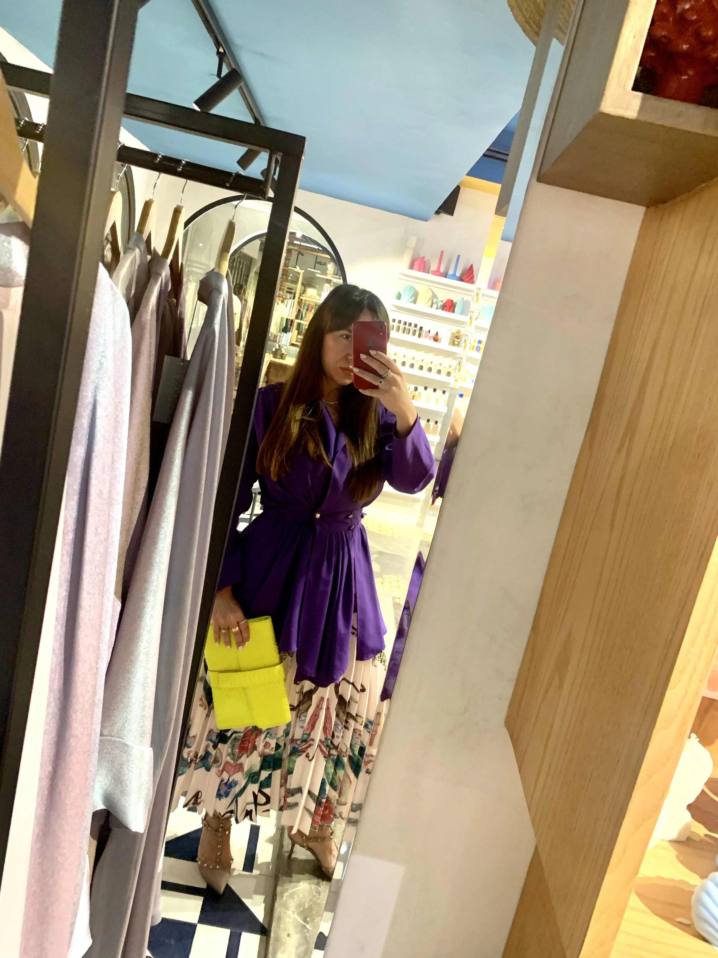 A woman in a purple dress taking a selfie in a mirror, showing her holding a yellow bag, wearing Manuela Cavallero,Manuela Cavallero, personal stylist and personal shopper in Dubai, in a boutique mirror wearing a purple satin dress