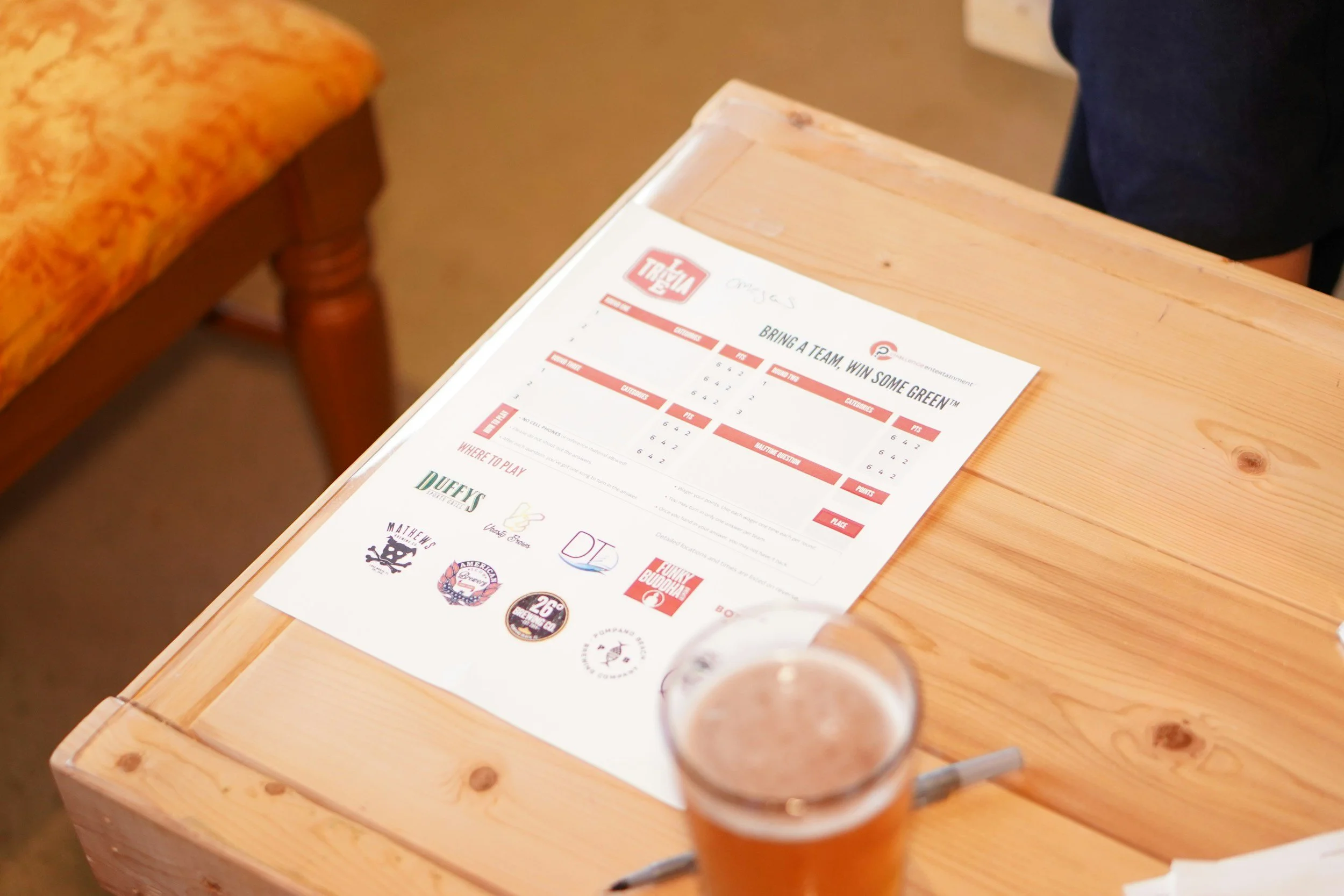 A table with a trivia game flyer, a pen, and a glass of beer.