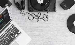 Laptop, vinyl record, record player, headphones, and music equipment on a white desk.