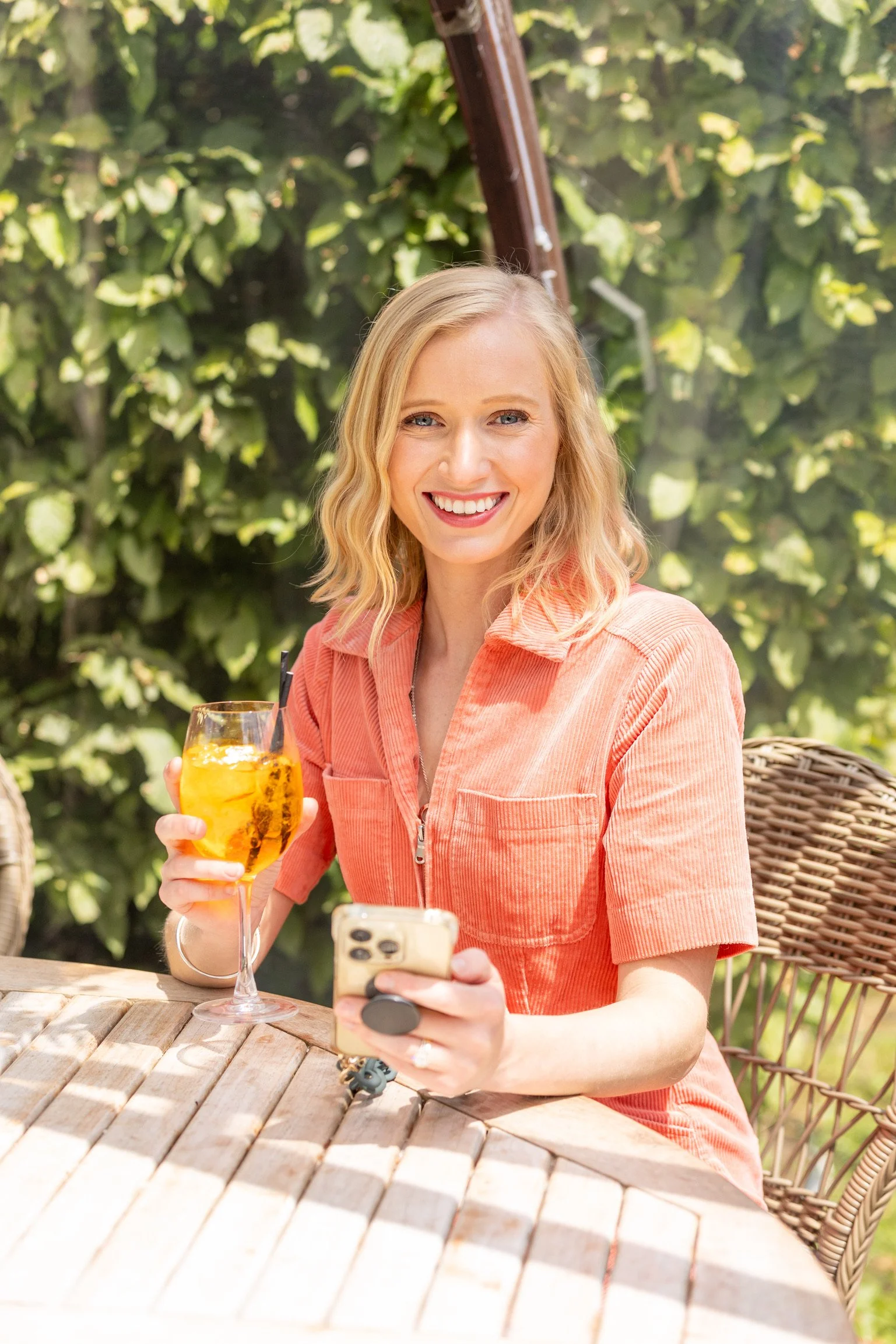 Robyn holding drink in front of green bush