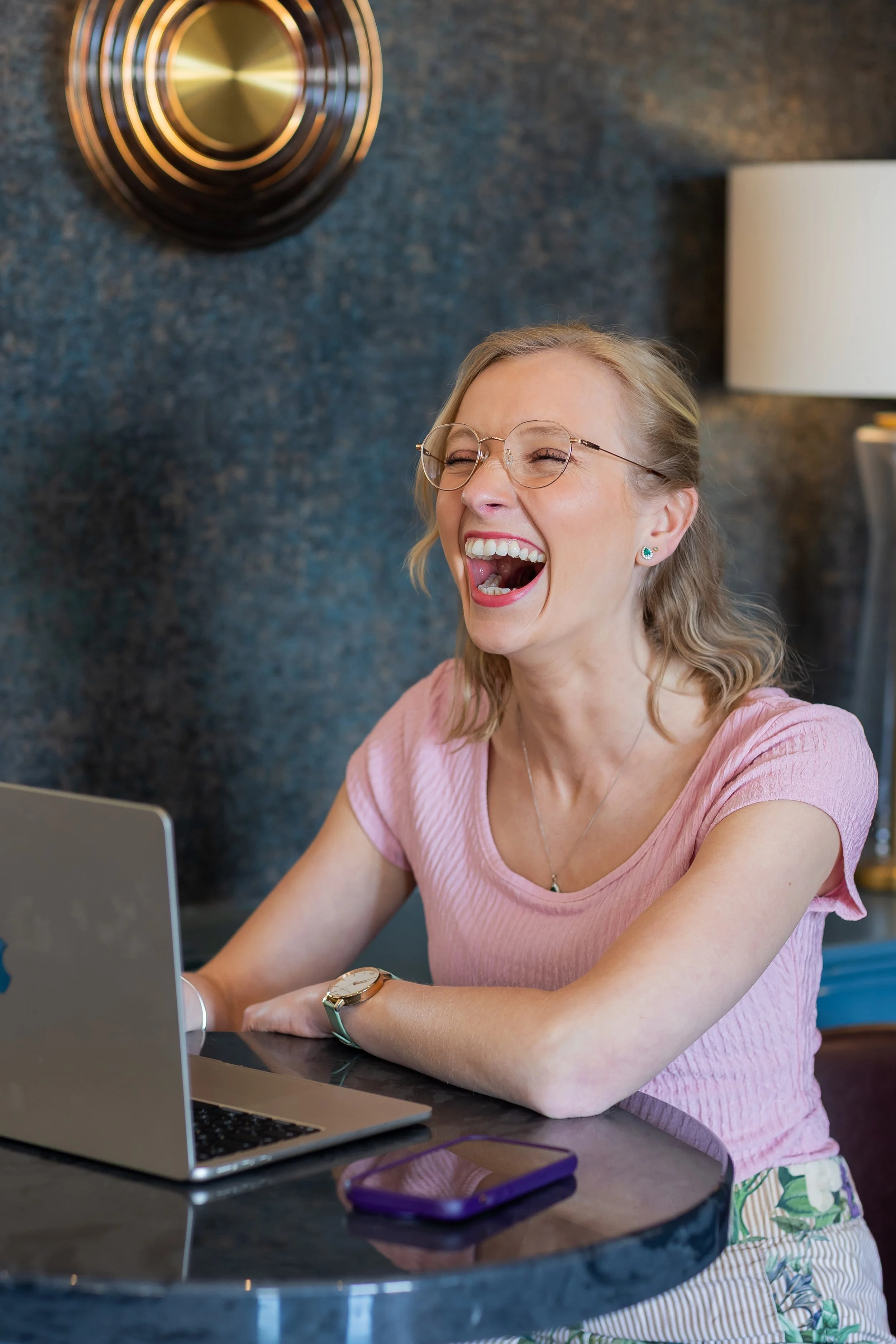 Robyn sat at a high table with a laptop and wide mouth genuine laughter