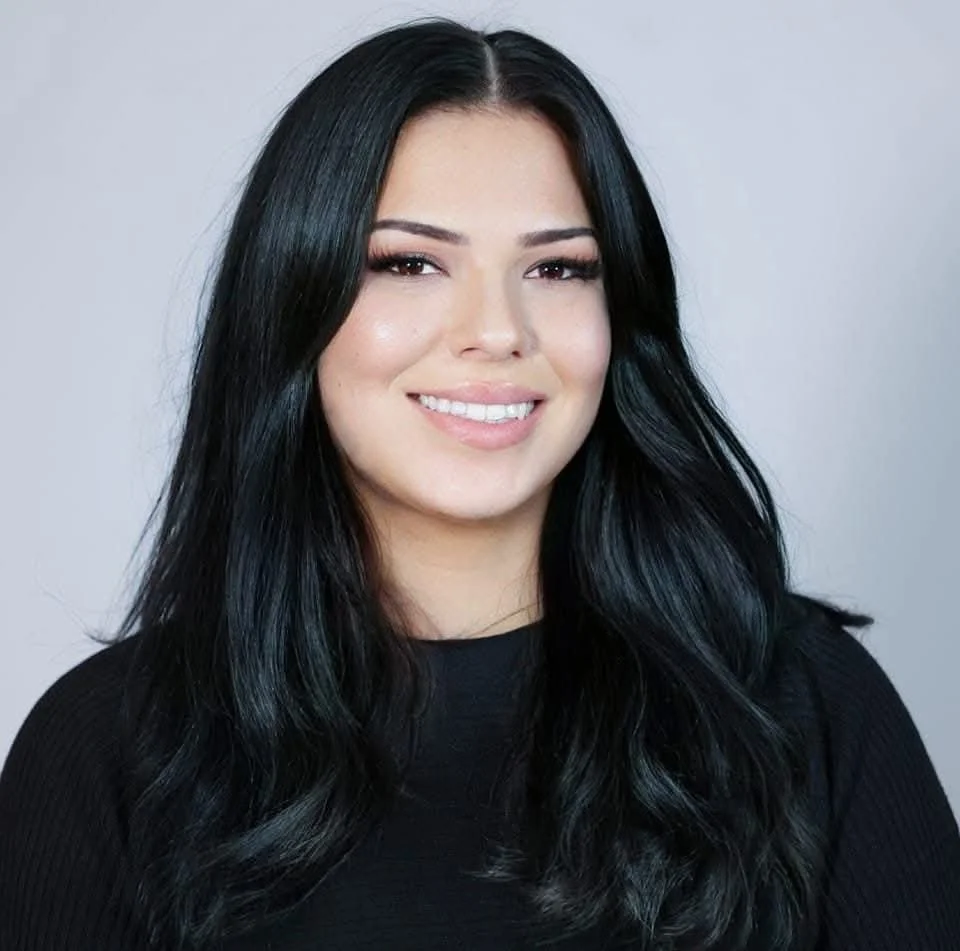 A woman with long dark hair wearing a dark blouse smiling at Vancouver Indigenous Fashion Week.