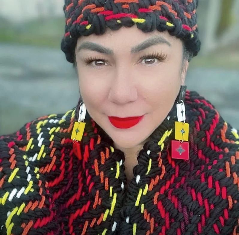 A woman wearing a matching yellow, orange, and red patterned hat and shawl, smiling at Vancouver Indigenous Fashion Week.