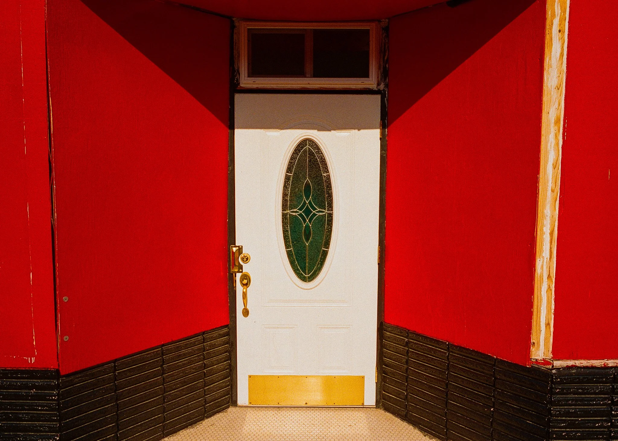 A front door with a decorative oval glass window, surrounded by red walls and black trim, with a brass handle and lock.