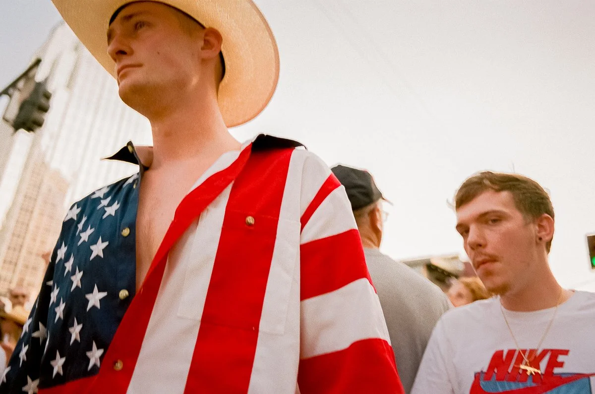 Young man wearing a patriotic American flag jacket and a wide-brimmed hat at an outdoor event