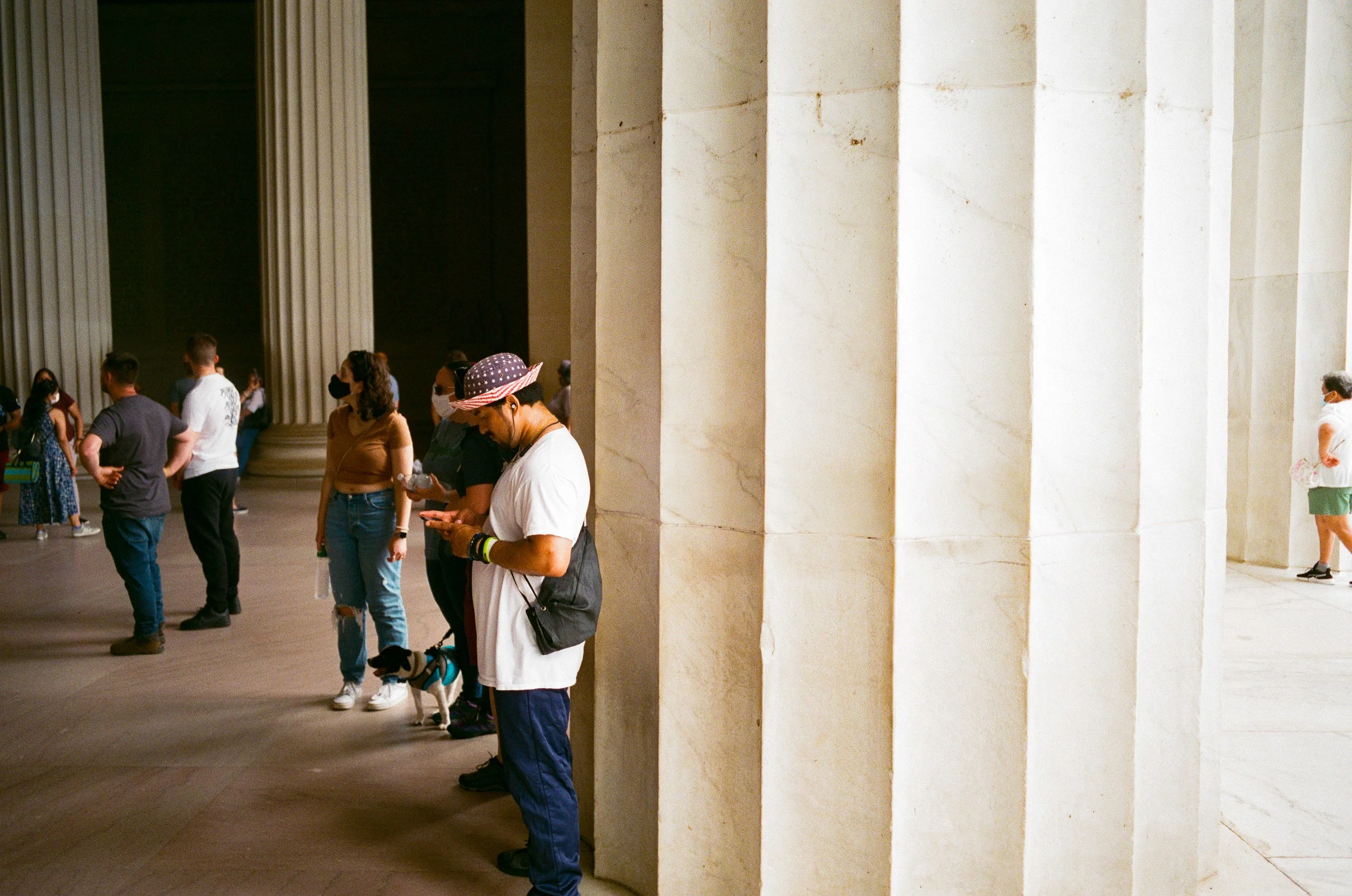 People standing in line near large marble columns at a museum, some wearing face masks.