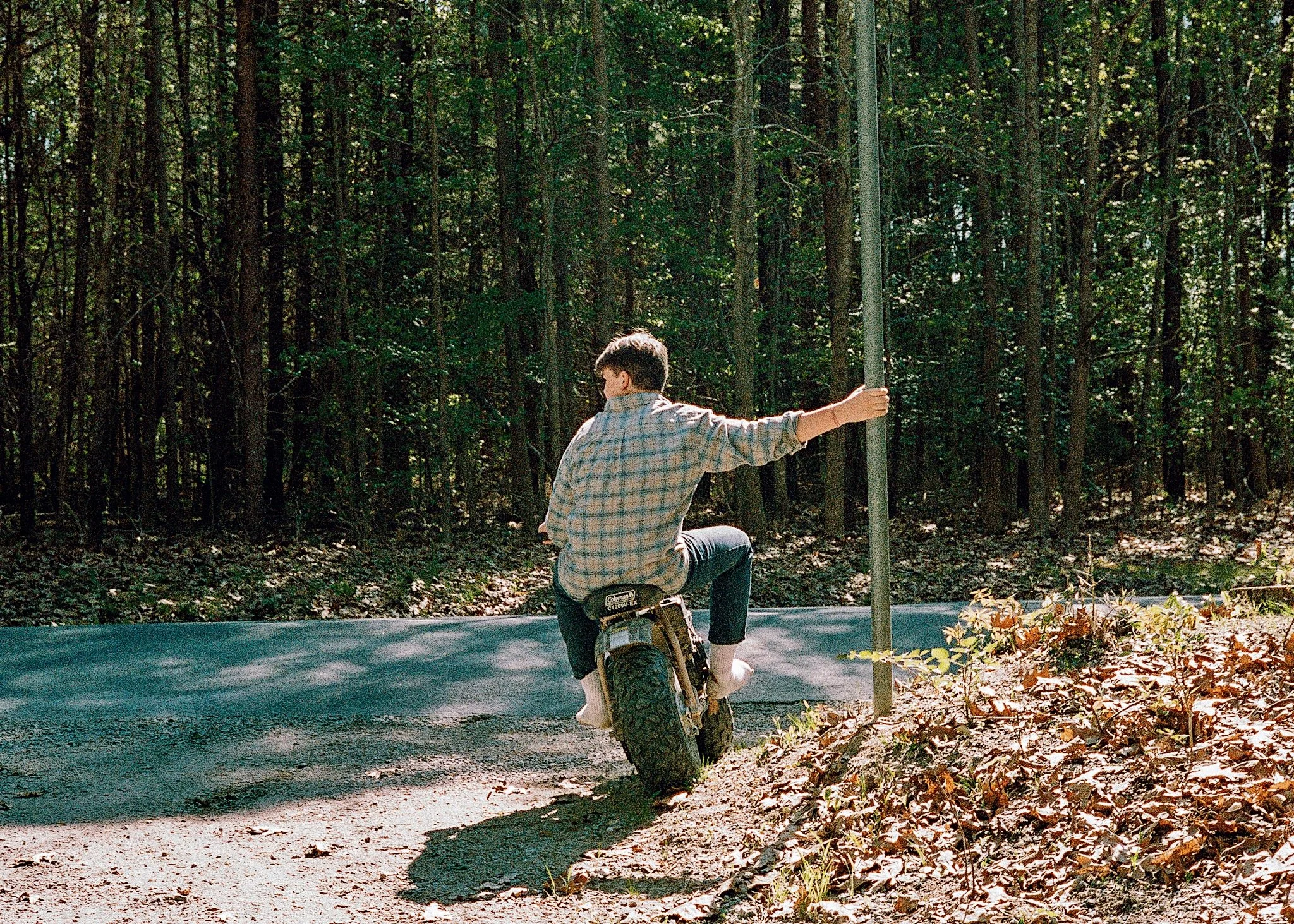 A young person riding a unicycle on a forest road, holding onto a pole for balance.