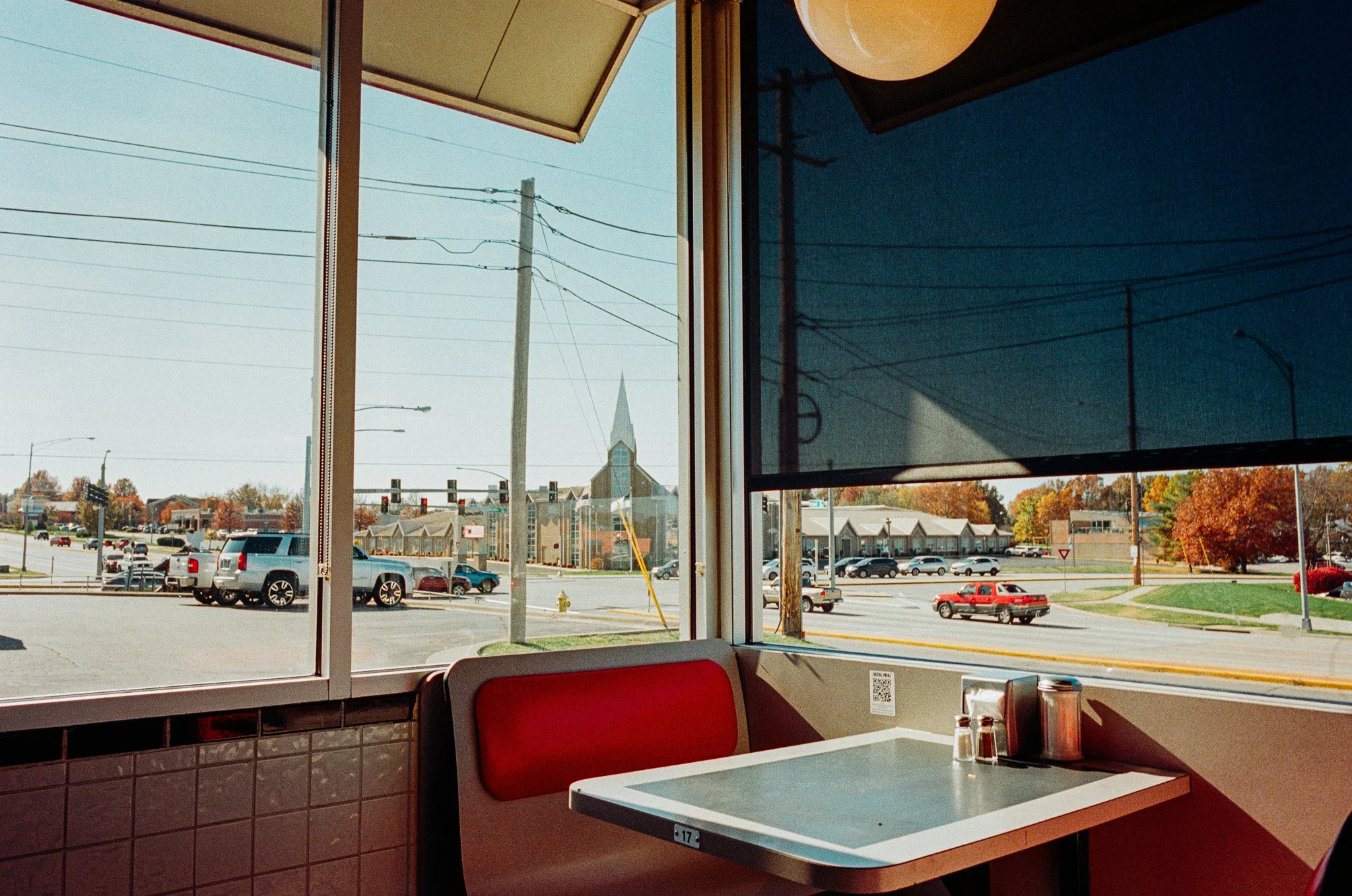 Interior view of a restaurant with a red booth seat near a window, showing a parking lot, street, and church outside on a sunny day.