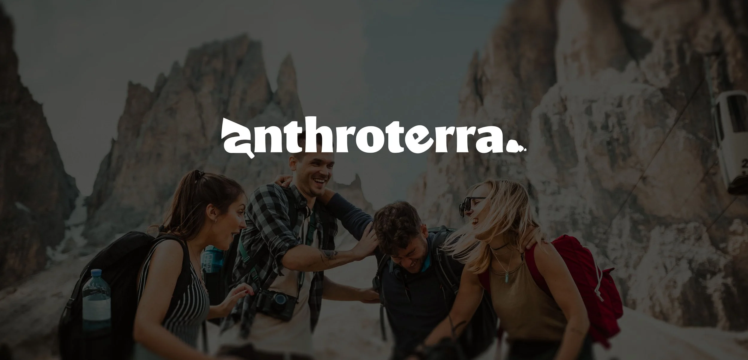 Group of young people hiking in a mountain landscape, smiling and interacting with each other, with snowy peaks and rocky cliffs in the background.