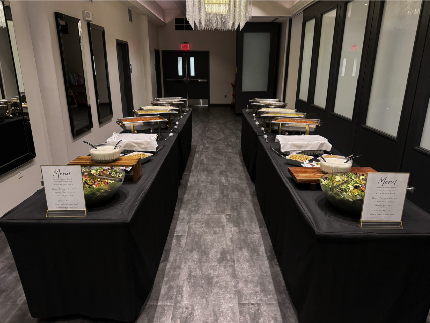 Buffet setup with chafing dishes and salads in a banquet hall with black tablecloths and modern decor.