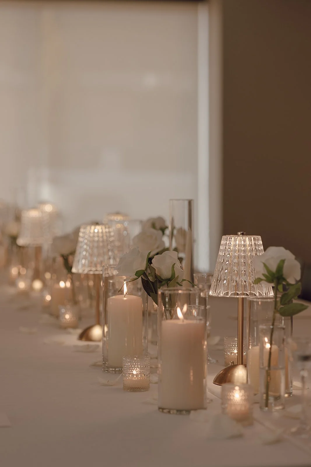 Elegant table setup with white flowers in vases, various candles, and decorative lamps with a softly lit ambiance.