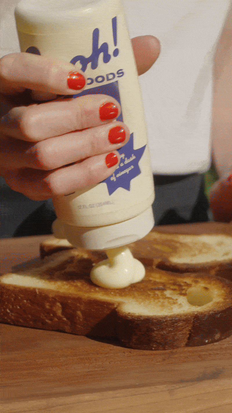 Person squeezing mayonnaise onto a toasted slice of bread with holes.