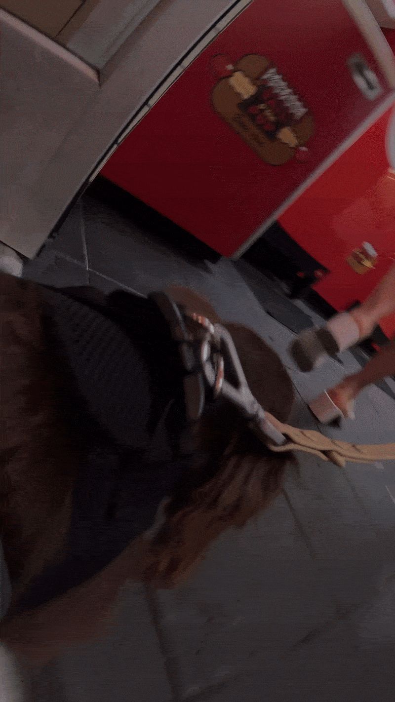 A dog wearing a harness lying on the floor in front of a hot dog stand.