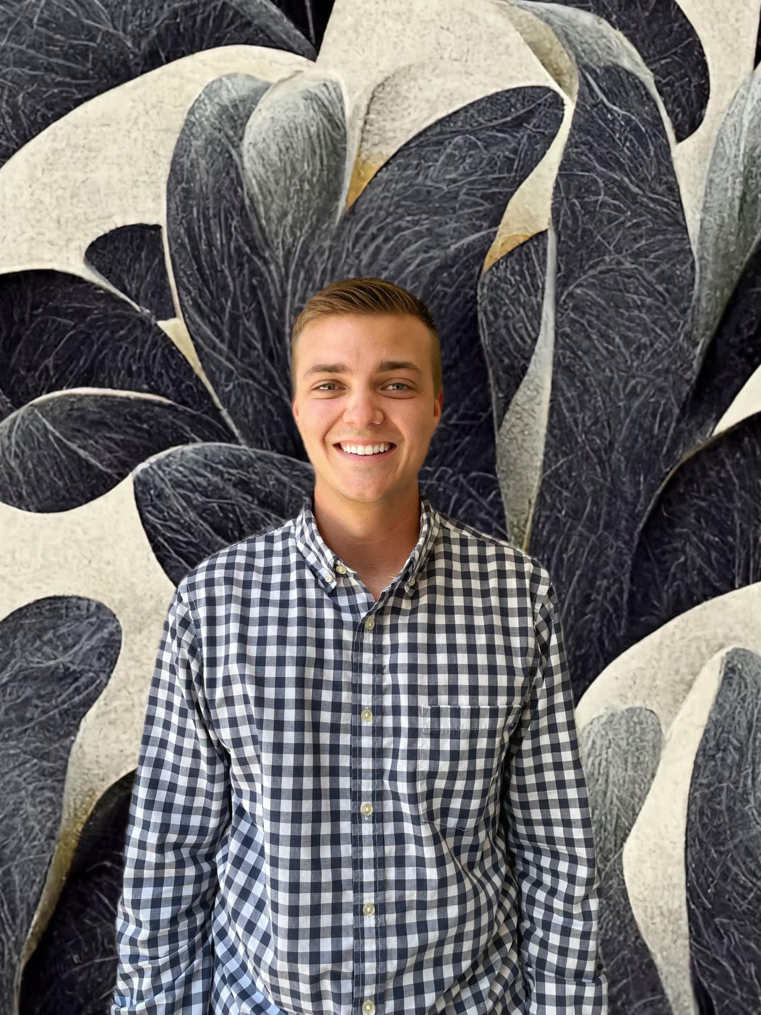 A young man smiling, wearing a black and white checkered shirt, standing in front of a large abstract black, white, and gold mural or painting.