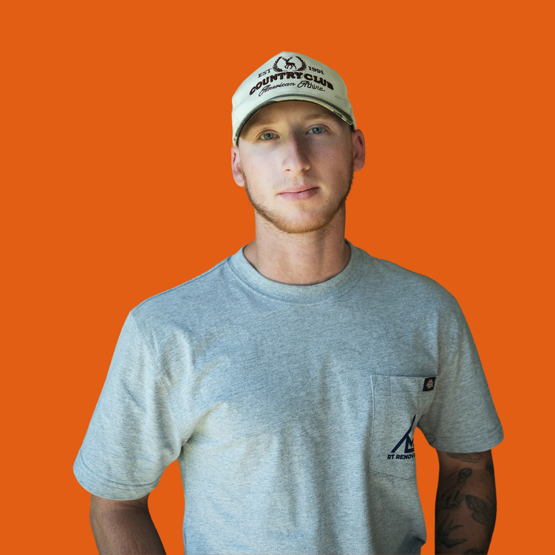 Jeffrey Speldrich who does job site support at RT Renovations. He has dark hair and a beard smiling, wearing a gray T-shirt with a logo on it, against an orange background.