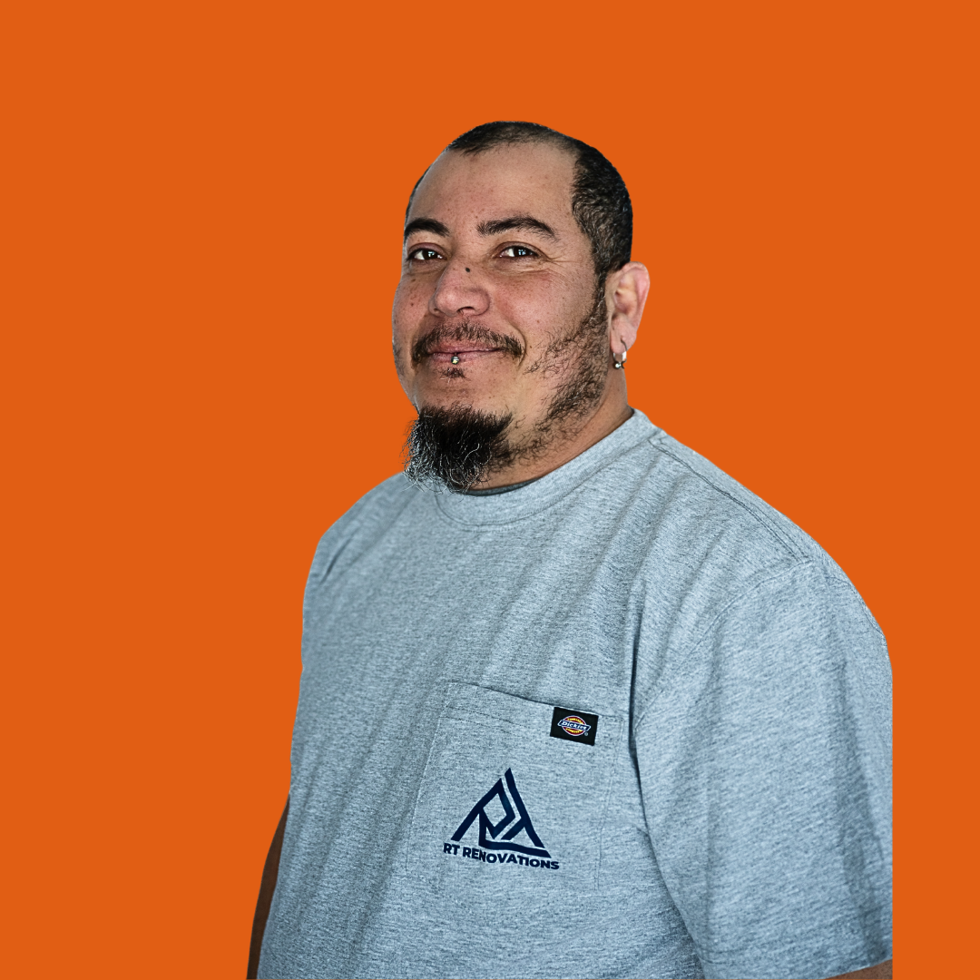 Person wearing a black cap and dark blue hoodie standing indoors against a white brick wall.
