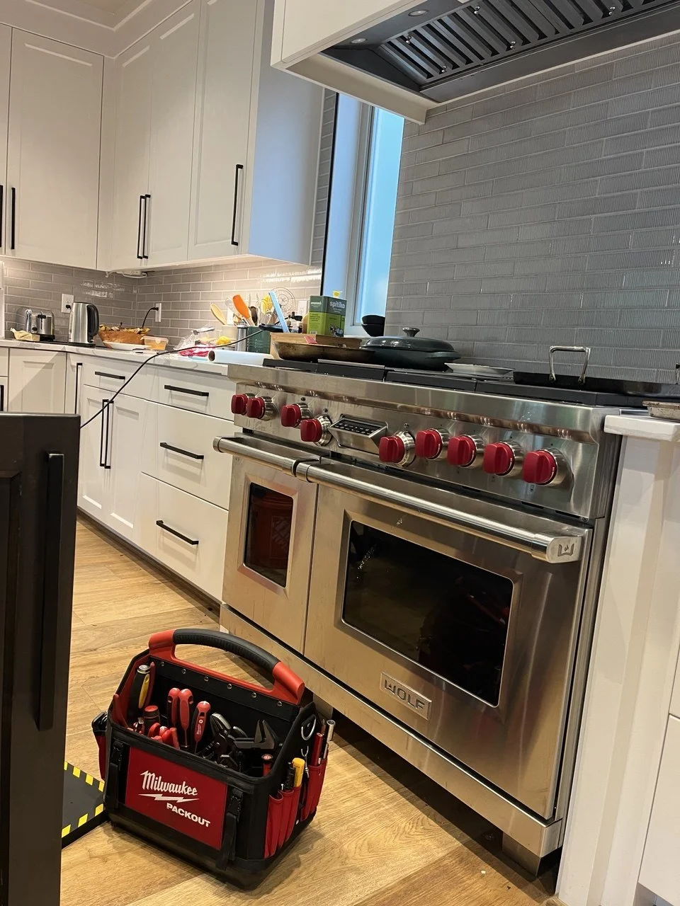 Kitchen with stainless steel stove, white cabinets, and a toolbox with tools on the floor.