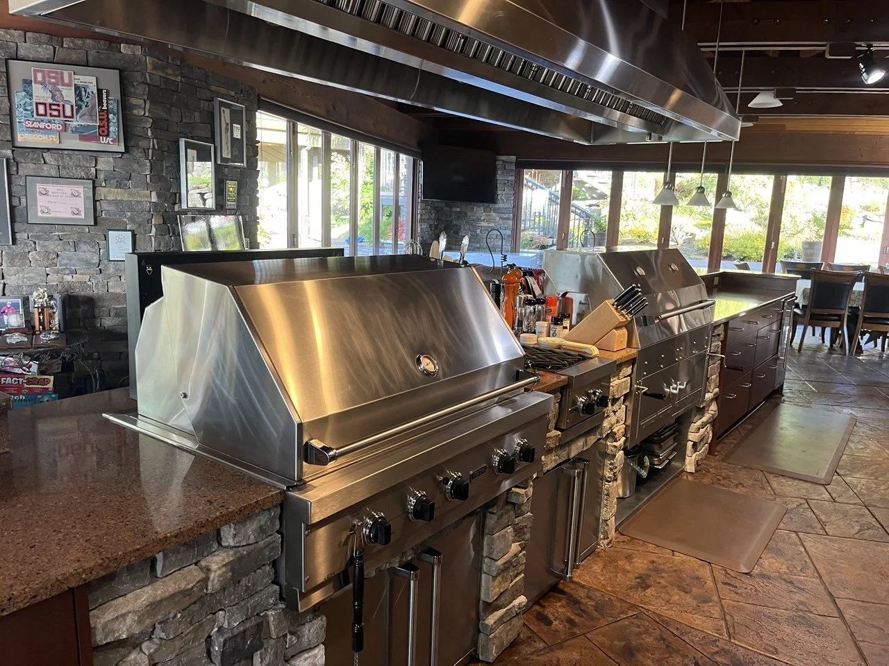 Commercial kitchen with stainless steel grills, countertop, and stone accents, near large windows in a restaurant setting.
