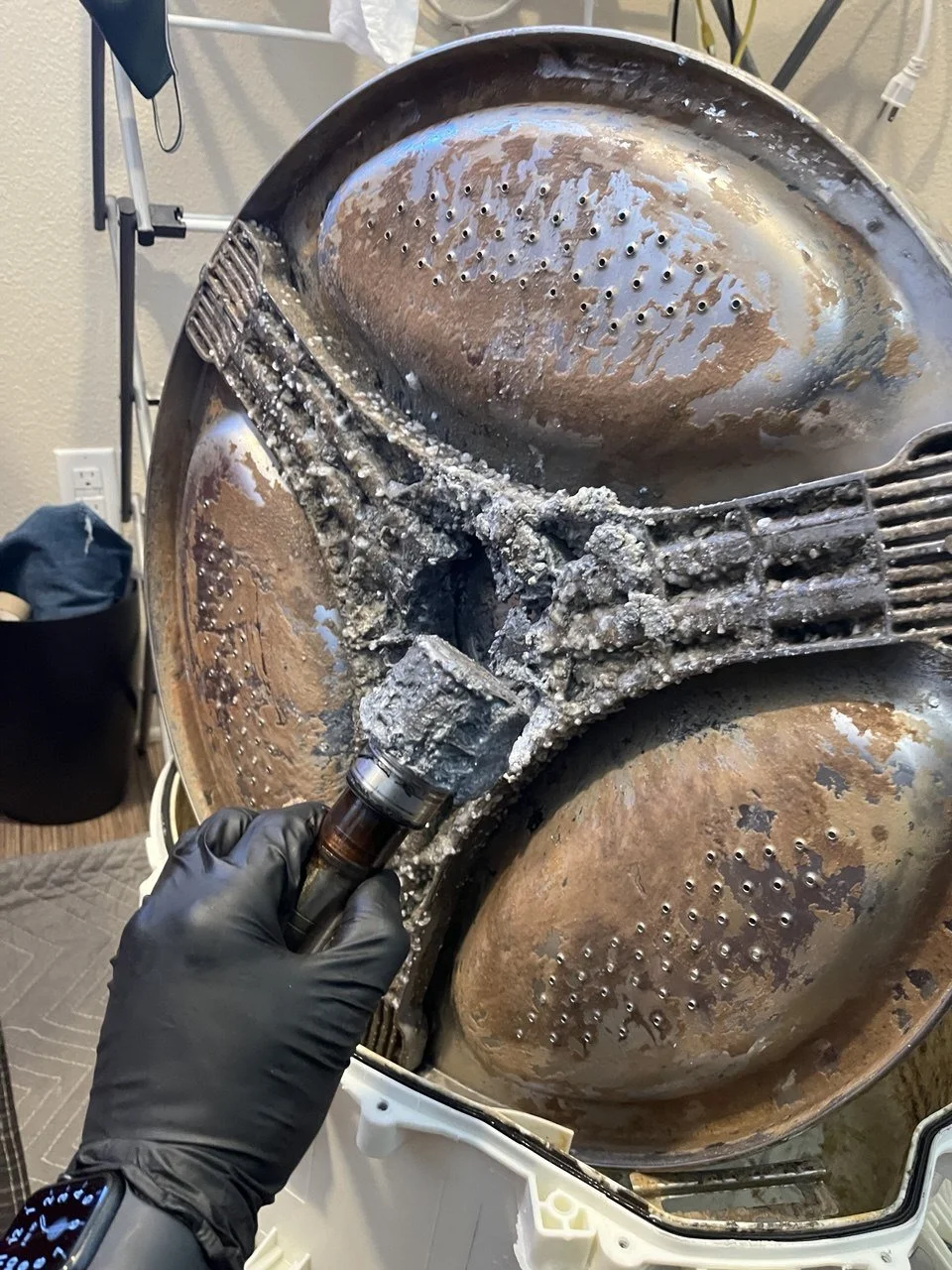 Investigating a heavily corroded and burnt coffee maker or kitchen appliance with a gloved hand holding a small tool.