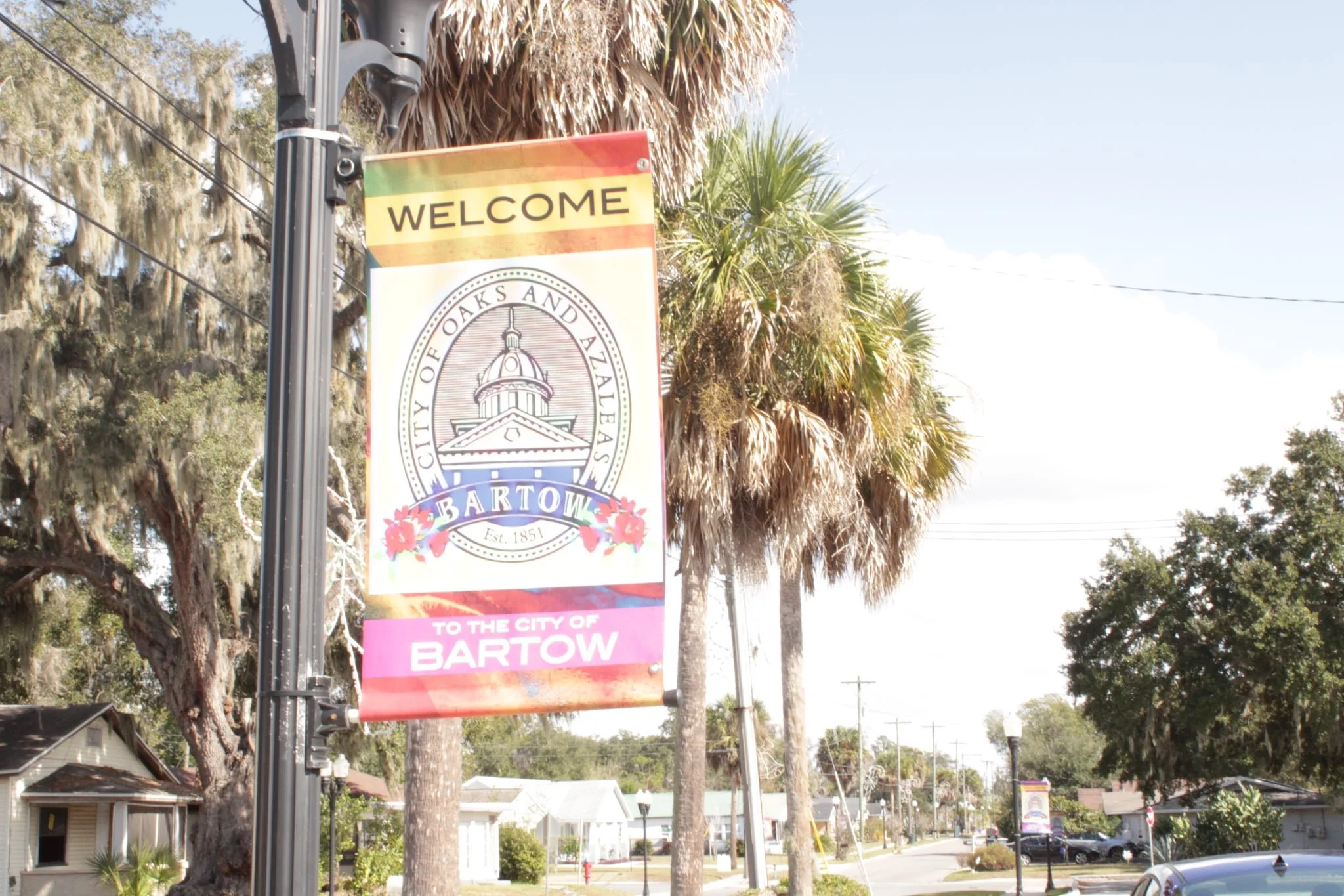 Welcome sign for the city of Bartow, with trees and houses in the background and power lines in the sky.