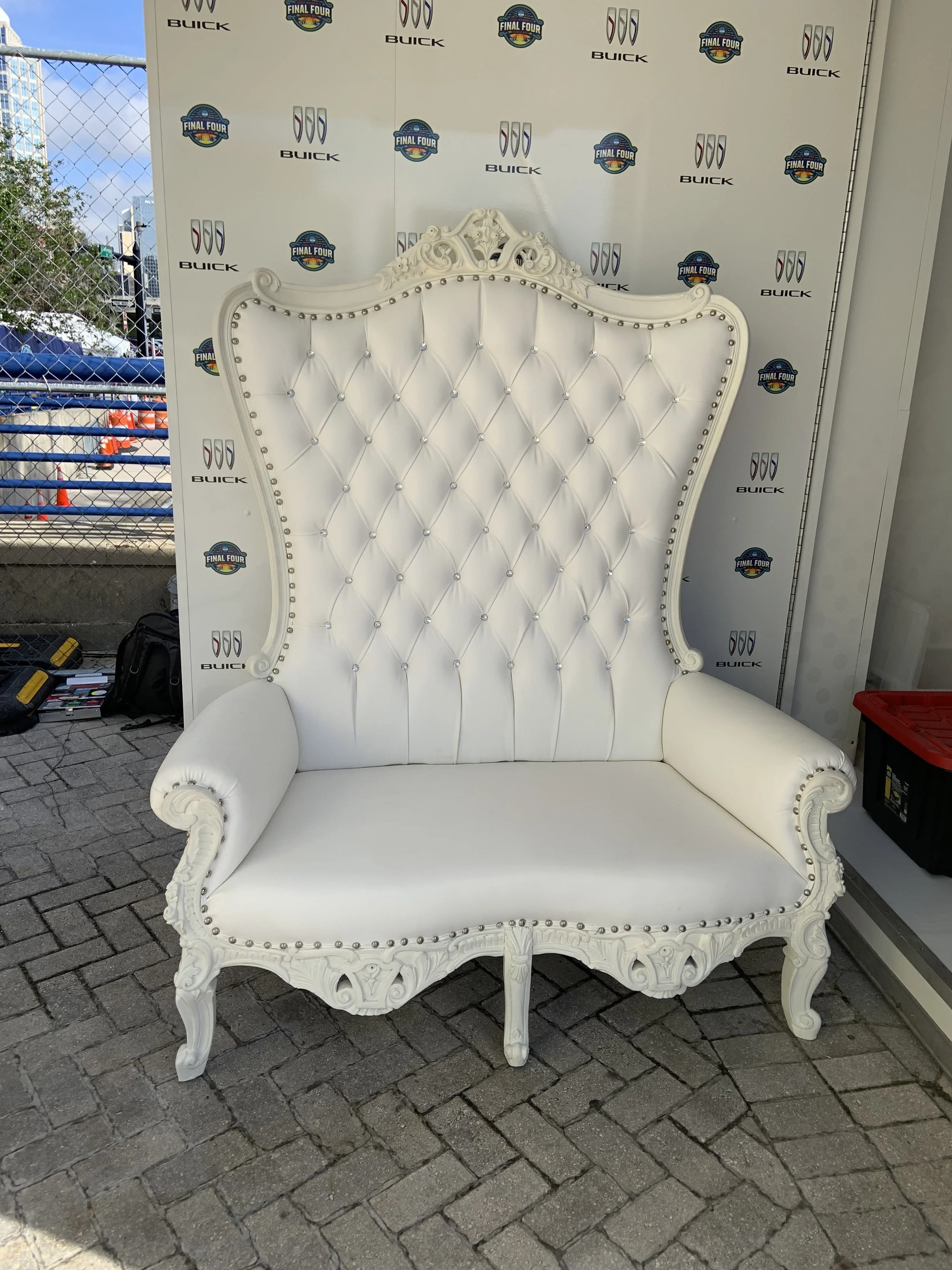 An ornate white high-backed chair with tufted upholstery, surrounded by logos of Buick and the Final Four.