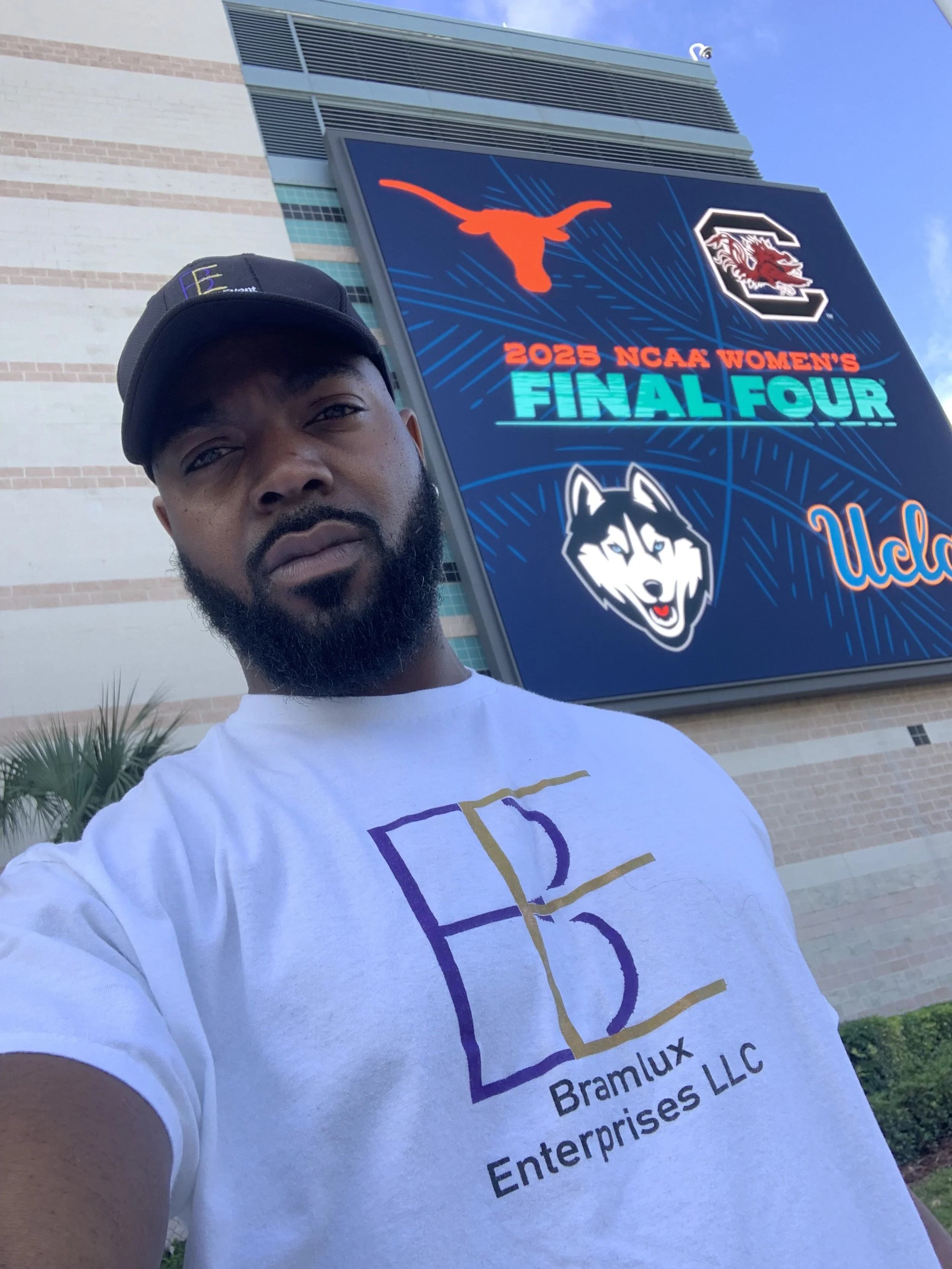 Man taking a selfie in front of a large digital billboard displaying the 2025 NCAA Women's Final Four logos for the University of Texas and the University of South Carolina, with the word "UCLA" partially visible.