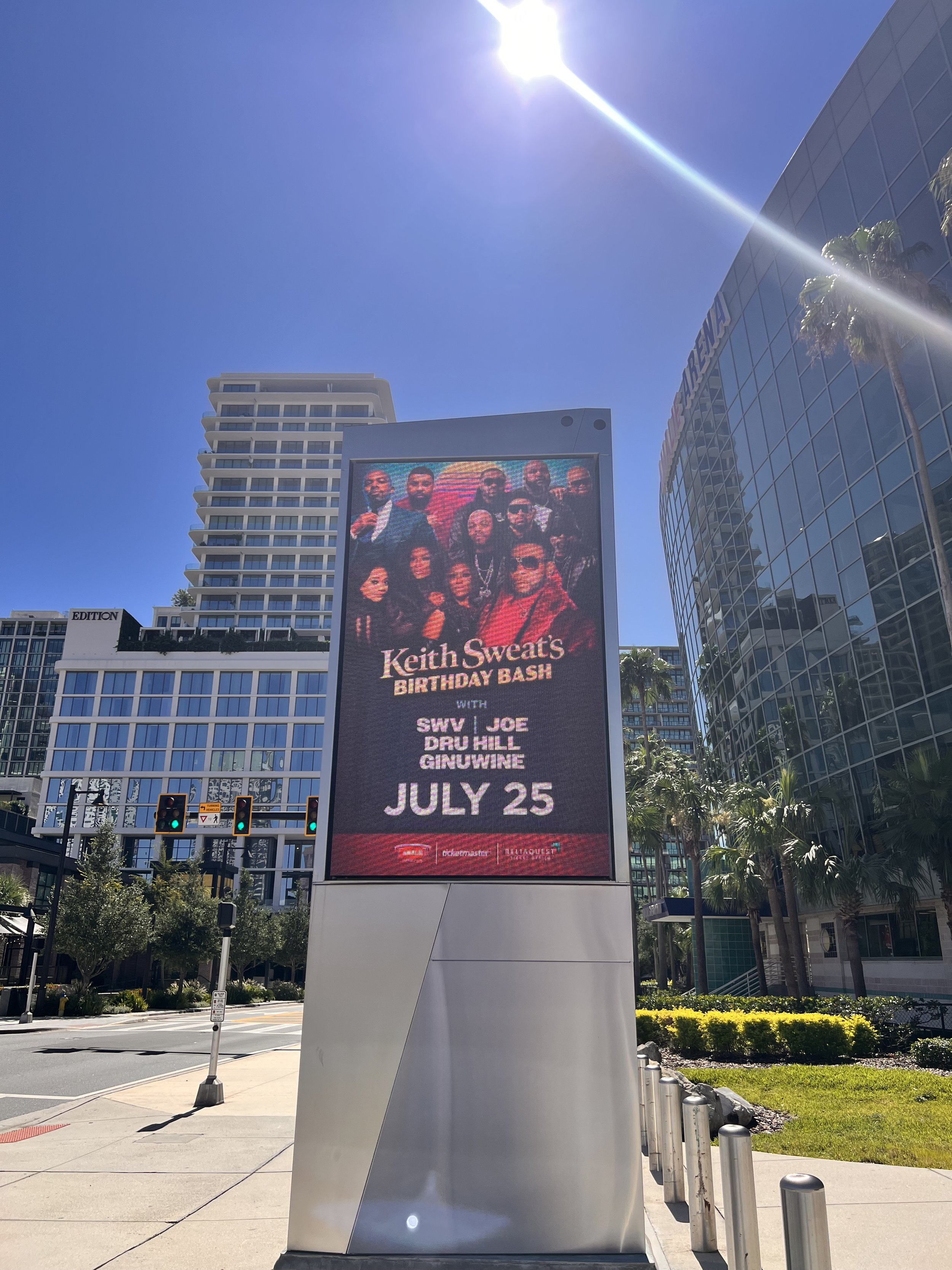 Digital billboard advertising Keith Sweat's birthday bash concert featuring SWV, Joe, D'Angelo, Dru Hill, and Ginuwine on July 25, located in a city with tall buildings, palm trees, and traffic lights.