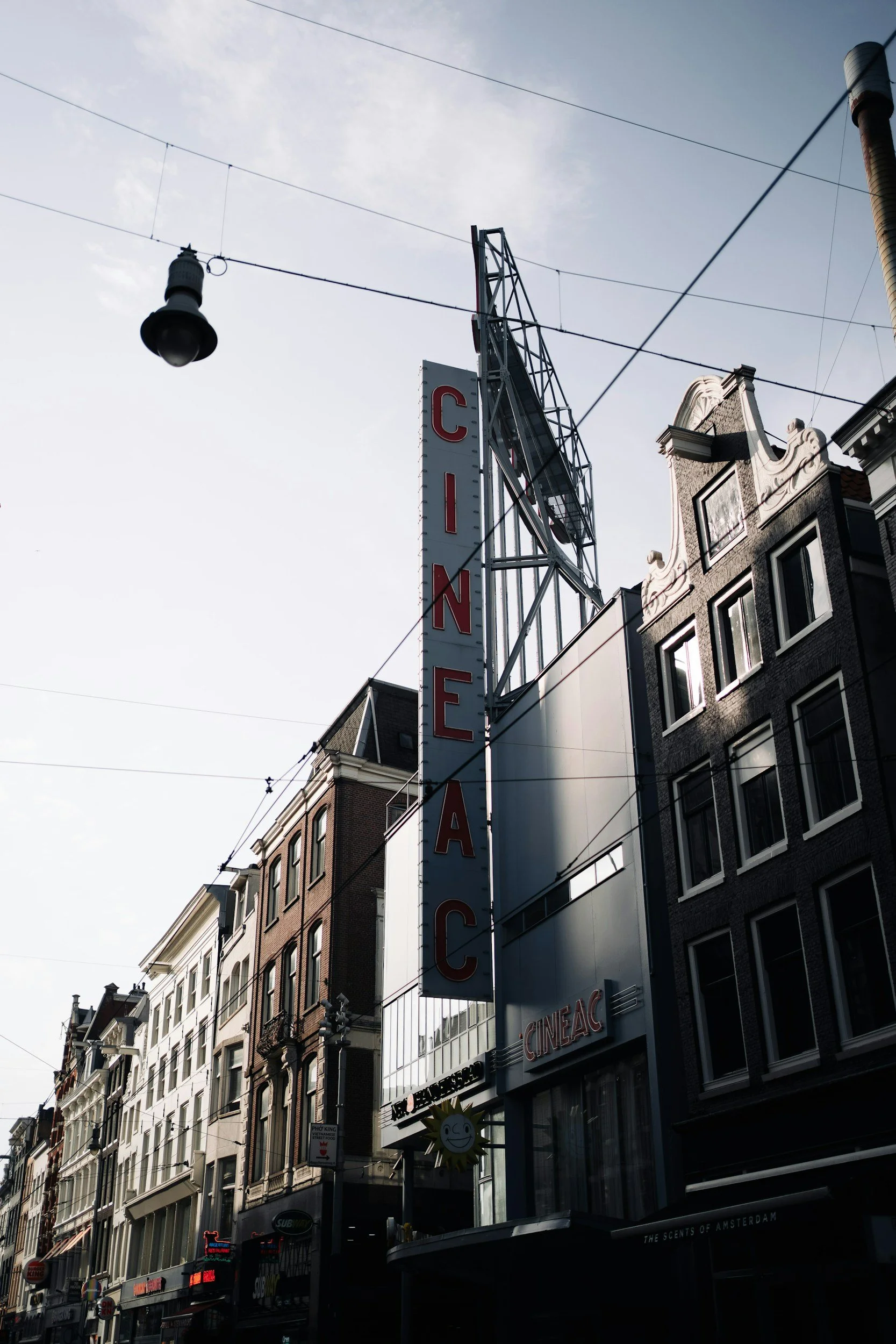 City street with tall buildings, a vertical sign reading 'CINEAC', and a sky with overhead power lines and a streetlamp.