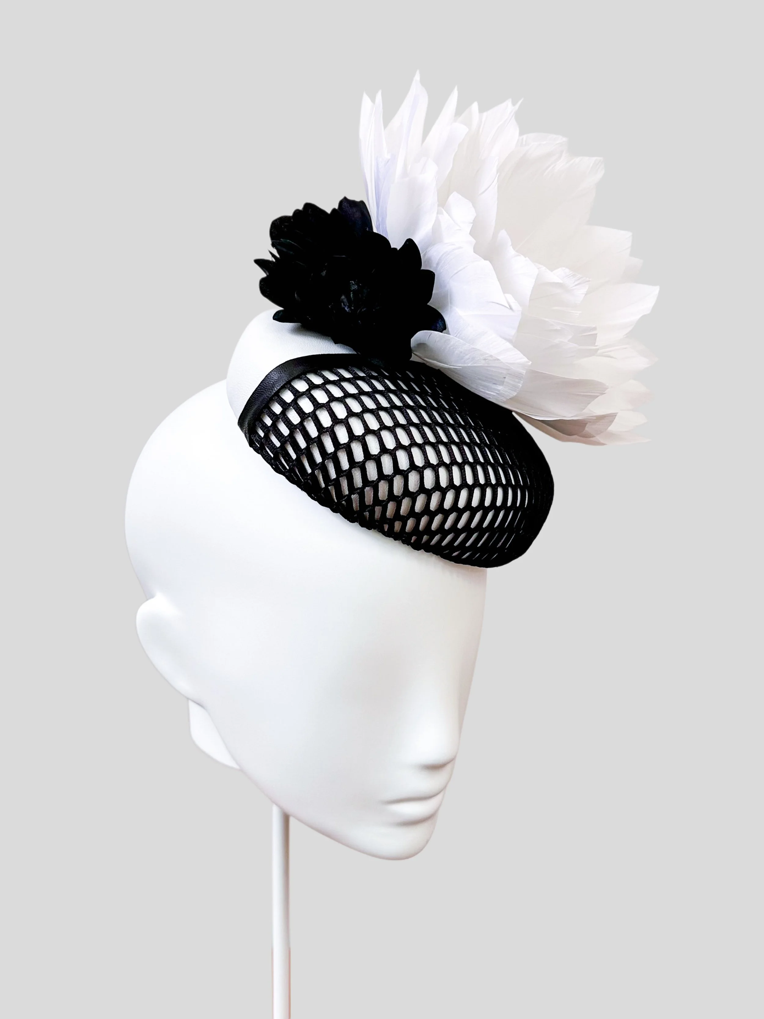 A left-side view of the Fiore Bianco cocktail hat, capturing the beautiful arrangement of the black silk buttercup flowers and the white feather flower.
