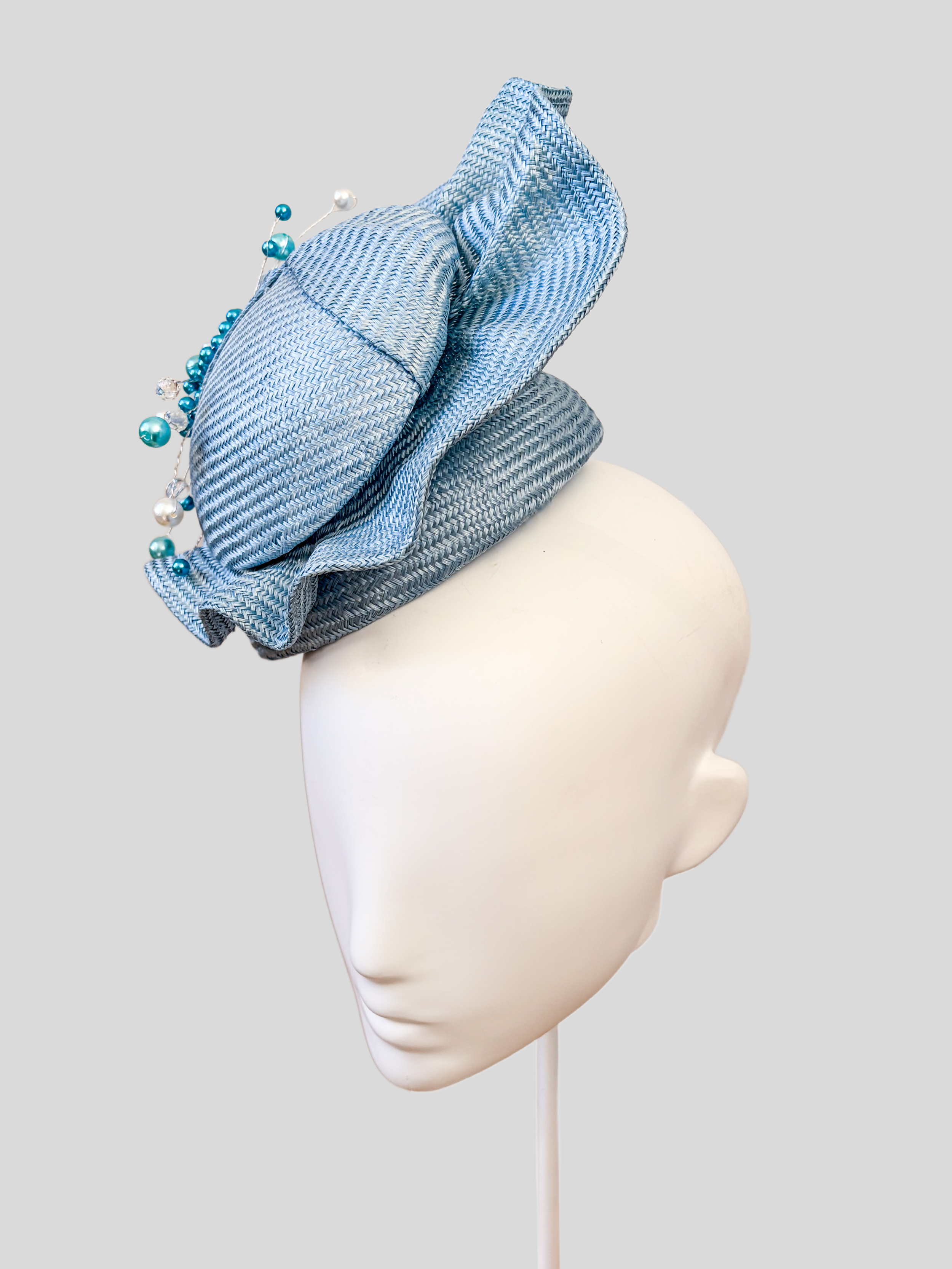 Right: Right-side view of the VÉRA Sky Parisisal cocktail hat highlighting its soft sky-blue finish and hand-beaded embellishment.