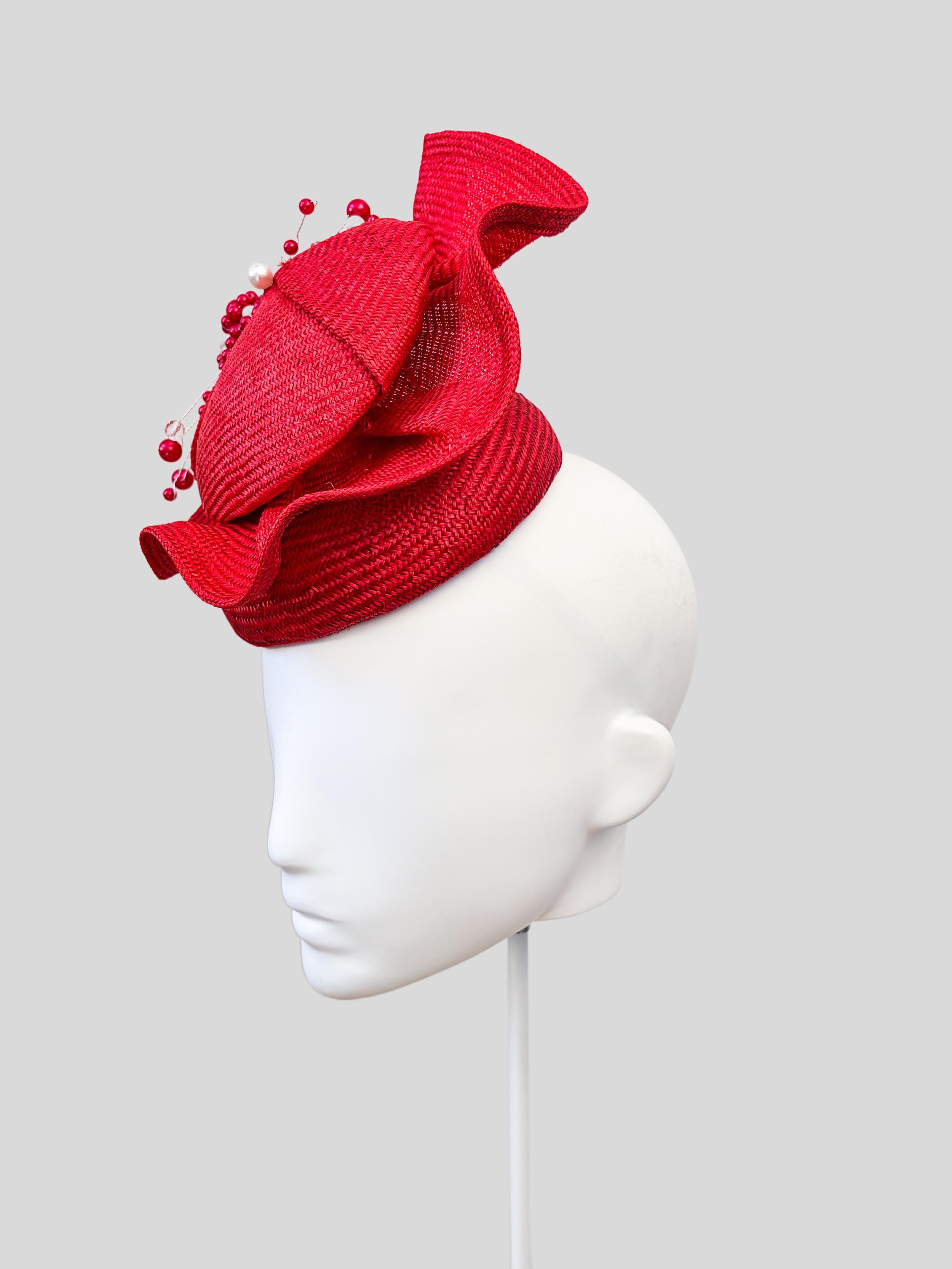 Right: Right-side view of the VÉRA Ruby Parisisal cocktail hat highlighting its vibrant ruby finish and hand-beaded embellishment.