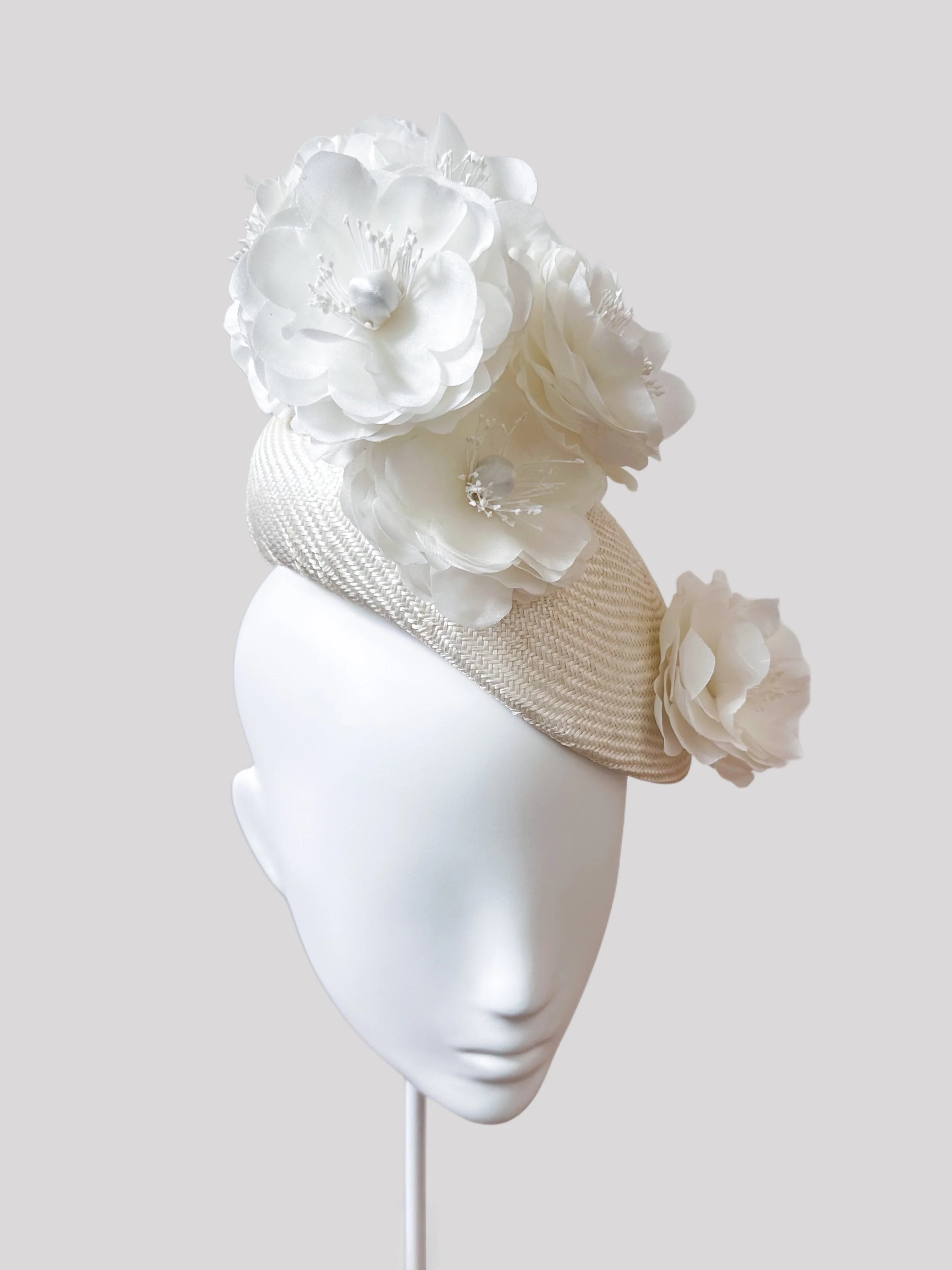 View of the Fiori Di Seta Avorio hat from the left side, highlighting its on-trend "face hugger" style and the graceful arrangement of its handmade flowers.