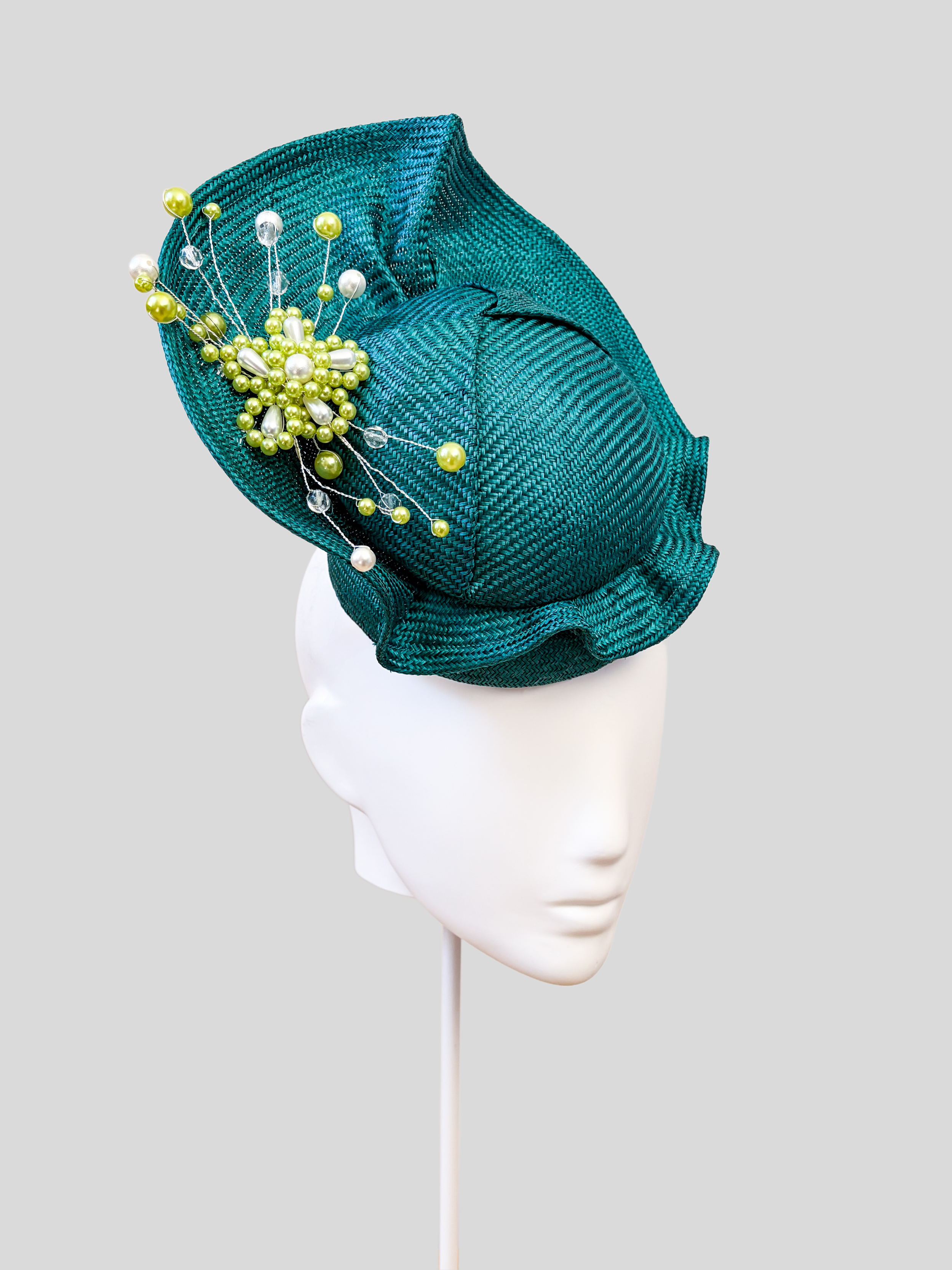 Left: Side view of the VÉRA Teal Parisisal cocktail hat showcasing its sculptural floating crown and rounded silhouette.