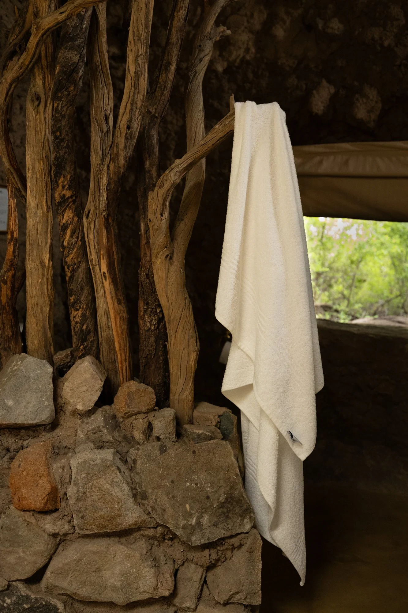 A white towel hanging on a wooden branch in a rustic setting with rocks and a stone wall.