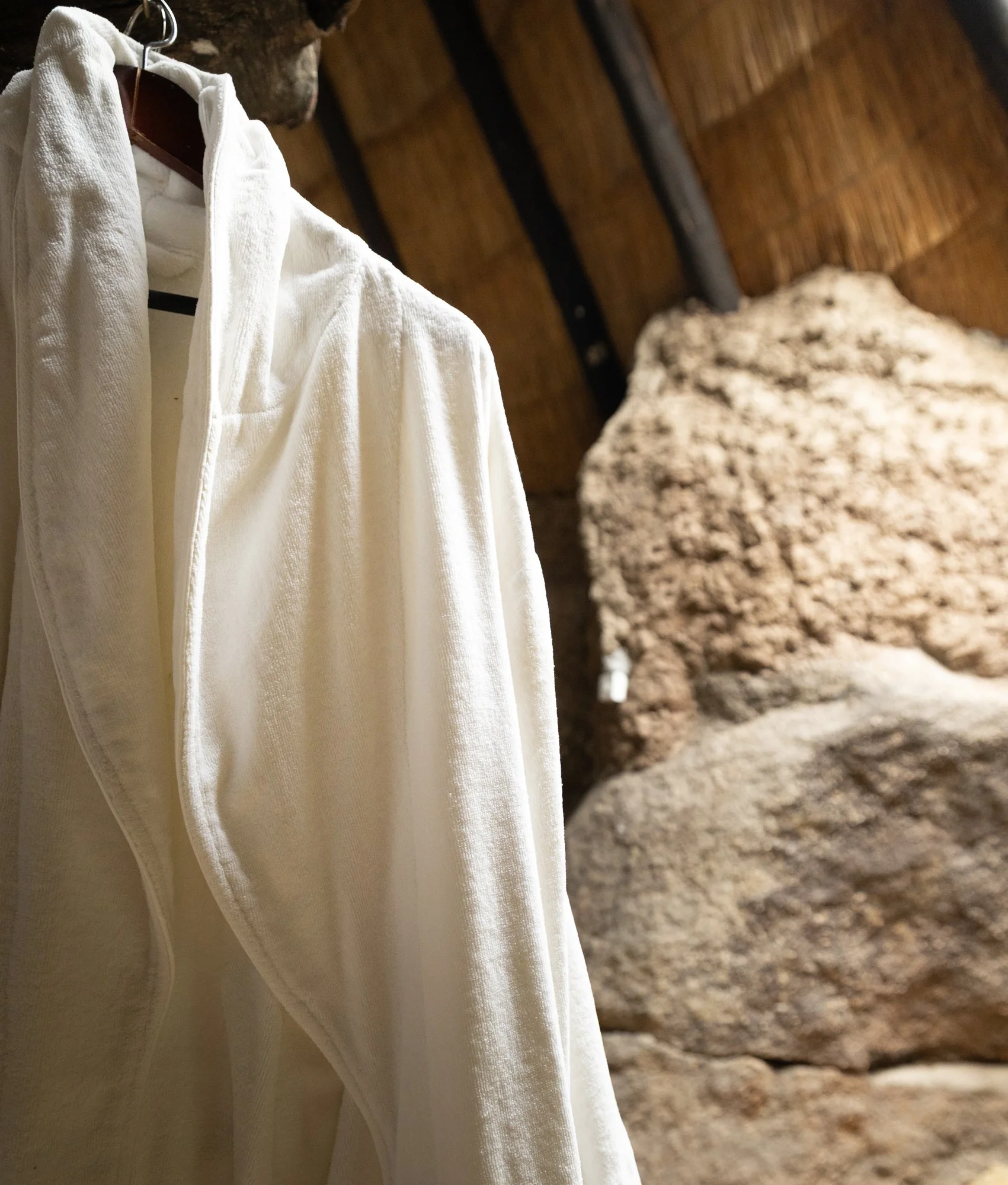 A white textured jacket hanging on a hanger in front of a wooden wall with exposed logs.