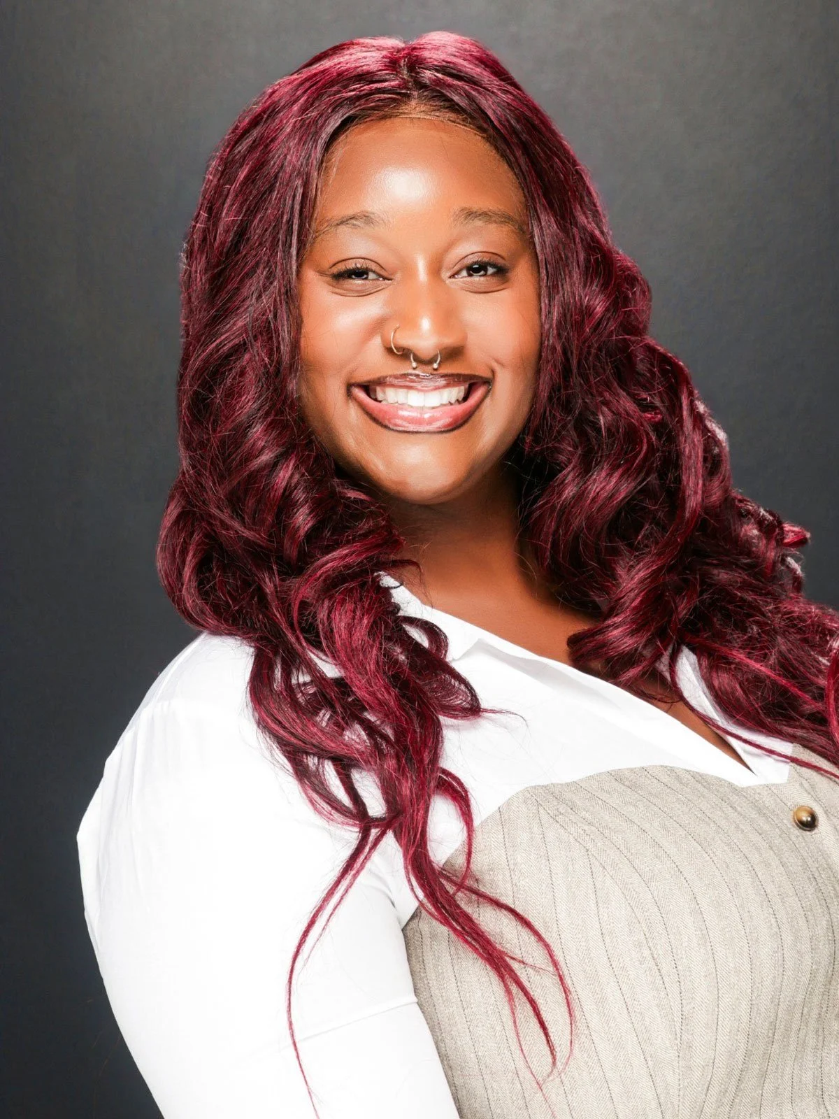 A woman with red hair smiling, turning towards the camera over her right shoulder, and leaning back slightly