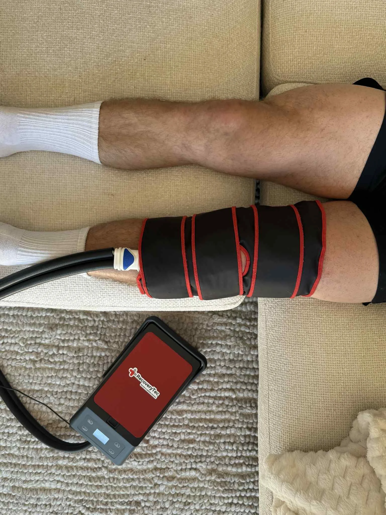 Person lying on the floor with a cold compression cryopush macine device on their leg connected to a portable pump.