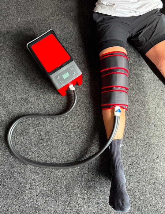 Person lying on the floor with a blood circulation device on their leg connected to a portable pump.