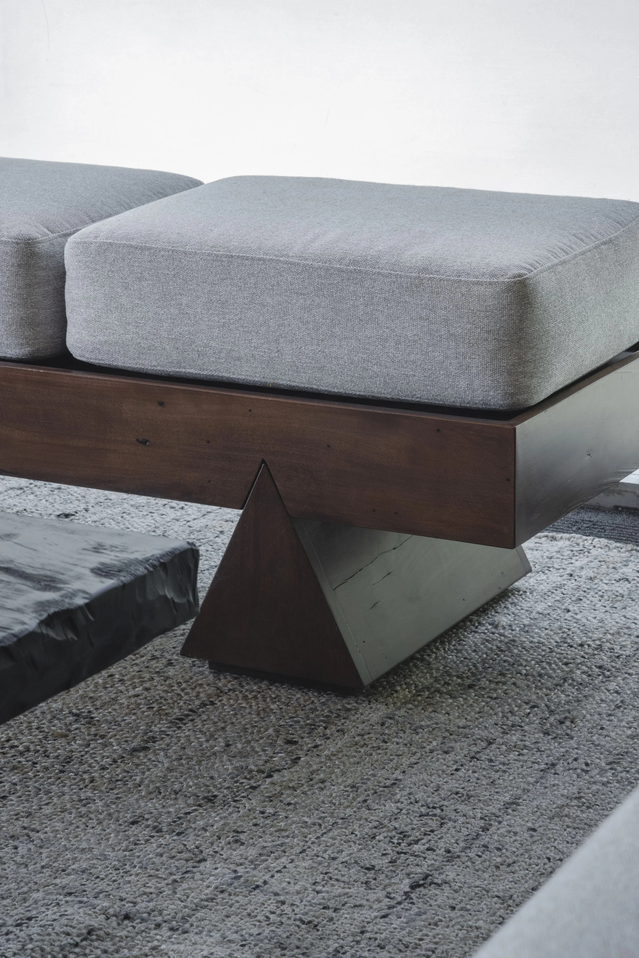 Close-up of a gray upholstered cushion on a dark wood mid-century modern bench or daybed frame.
